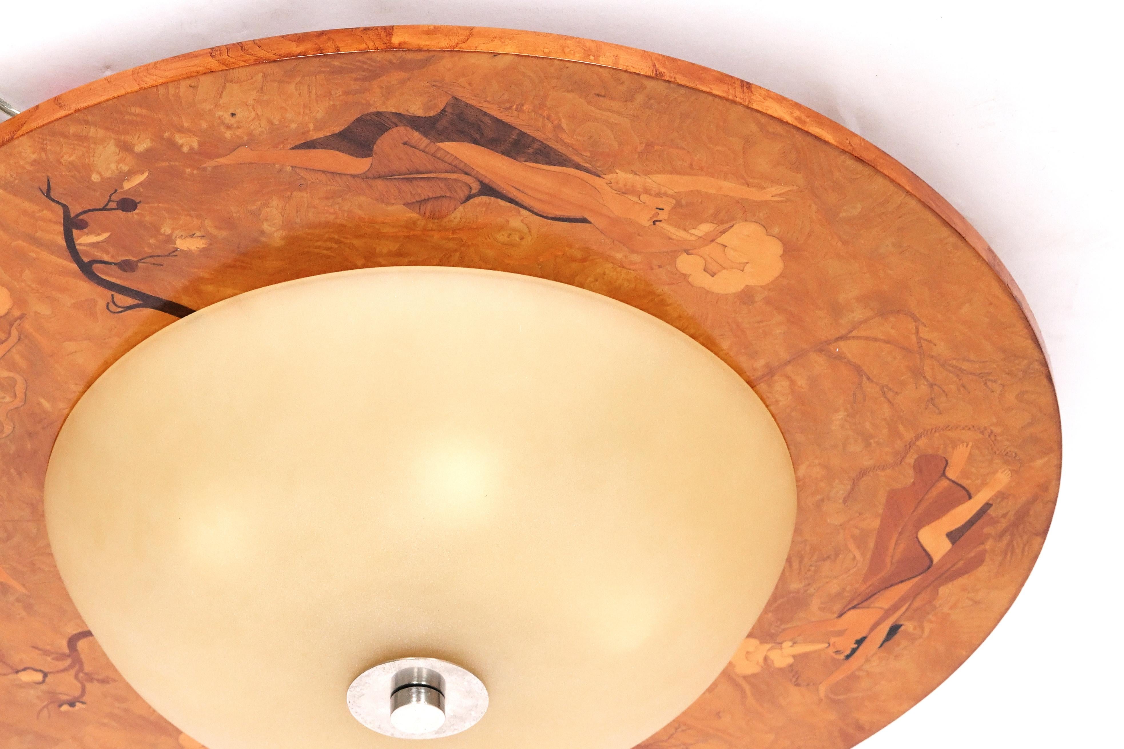 A Swedish grace period flush mount ceiling fixture with a round frame having figured birch veneer inlaid with figures depicting the elements inter-spurted with stylized trees. circa 1930s. The wooden frame has six medium sockets (100 watts LED or
