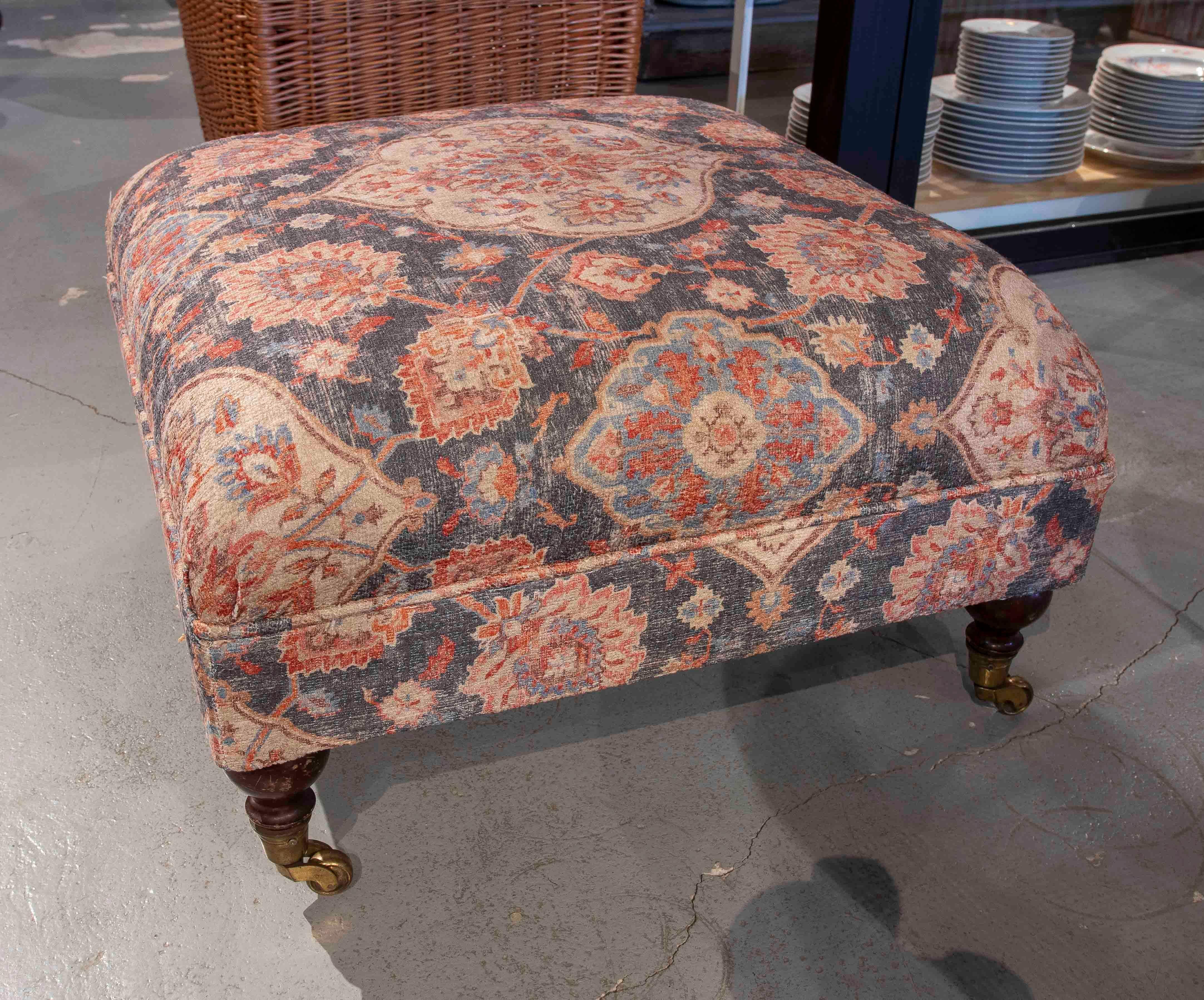 Ottoman bench with mahogany legs and bronze casters, upholstered in an oriental-inspired floral print.
