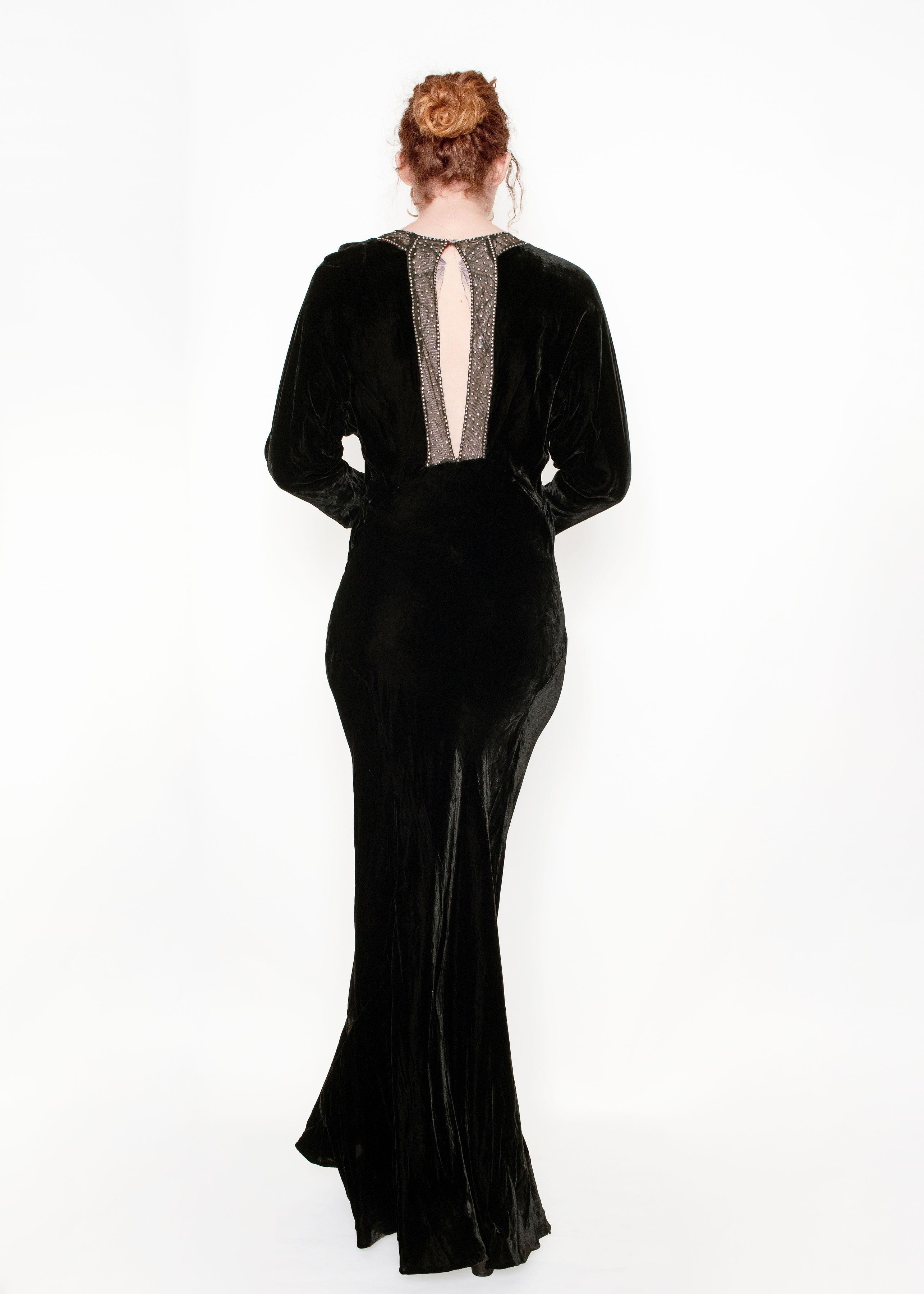 This 1930's velvet & rhinestone gown exudes sophistication, with its sheer chest featuring crystal detailing and full length sleeve with velvet buttons. The keyhold back opening and silhouette creates an elegant and timeless look. Perfect for any