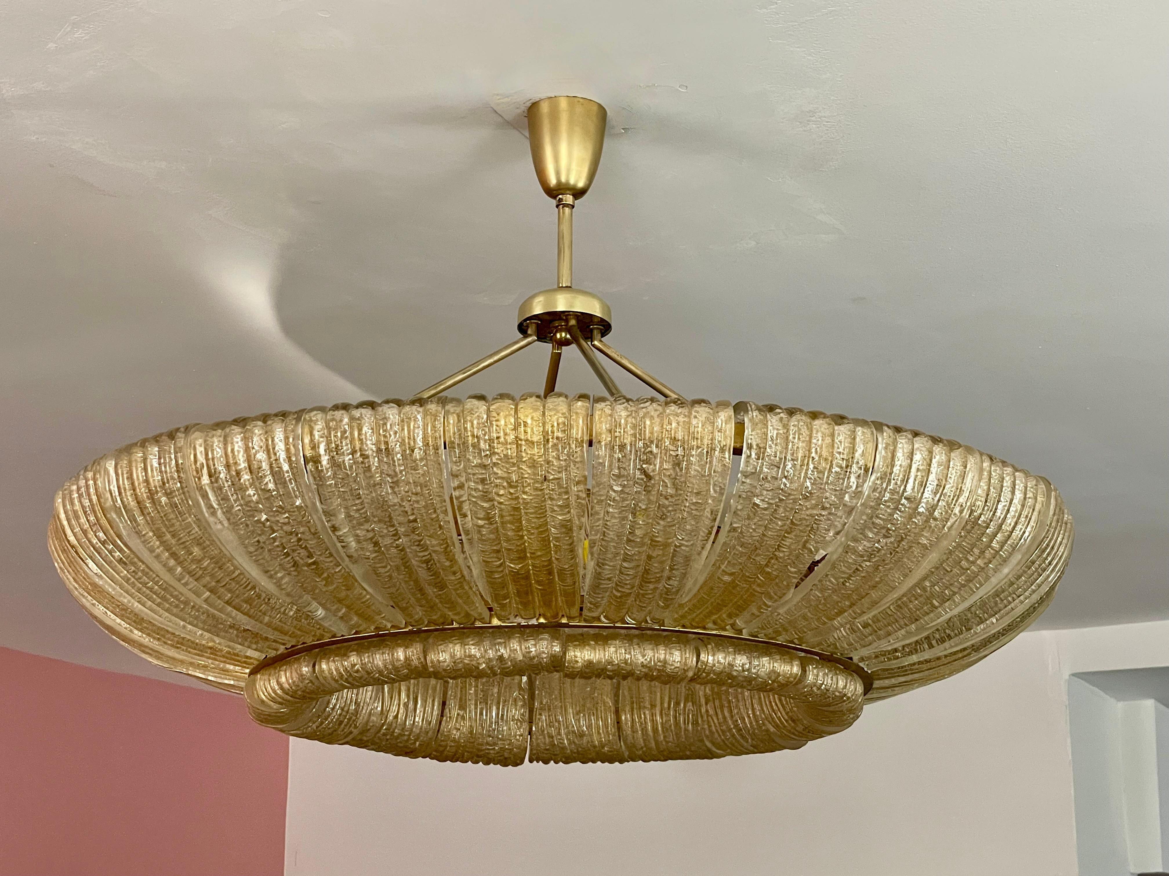 This late 1930s Venini chandelier has two rings of curved-glass elements suspended from a brass frame.  It appears to glow magically from within because the glass elements are infused with gold leaf.  Tiny glass chips are fused on the inner surface