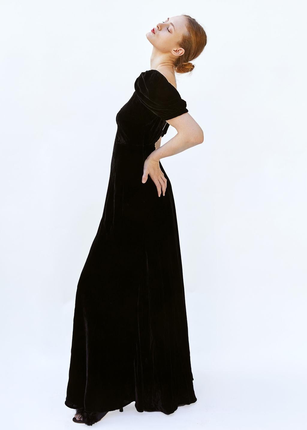 Step back in time with this captivating 1930s black velvet gown, exuding timeless elegance and sophistication. This exquisite piece features a square neckline that beautifully frames the collarbone and shoulders, giving a nod to vintage glamour. The