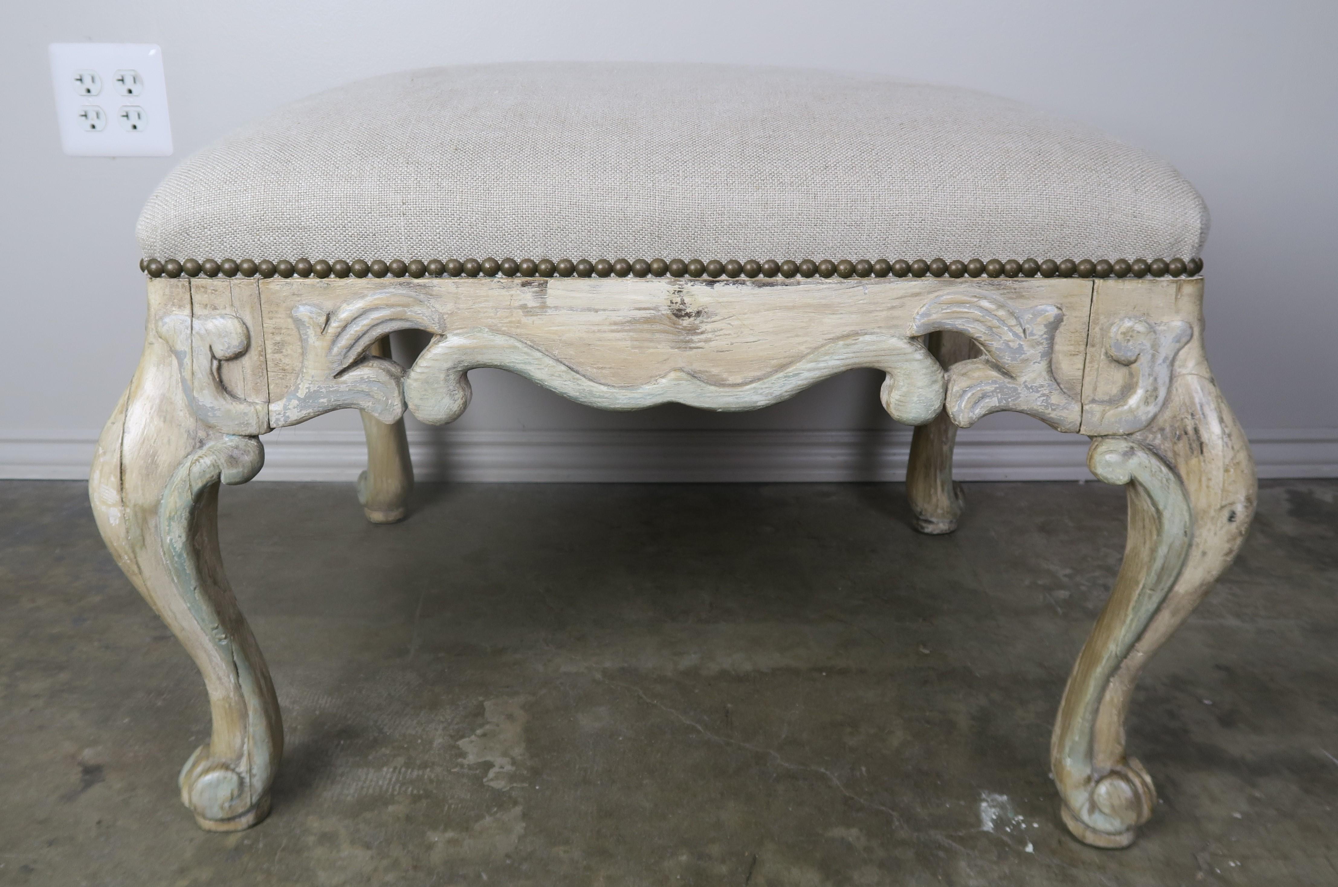 1930s French painted carved wood bench standing on four cabriole legs with ram's head feet. The bench is newly upholstered in washed linen with antique brass nailheads.