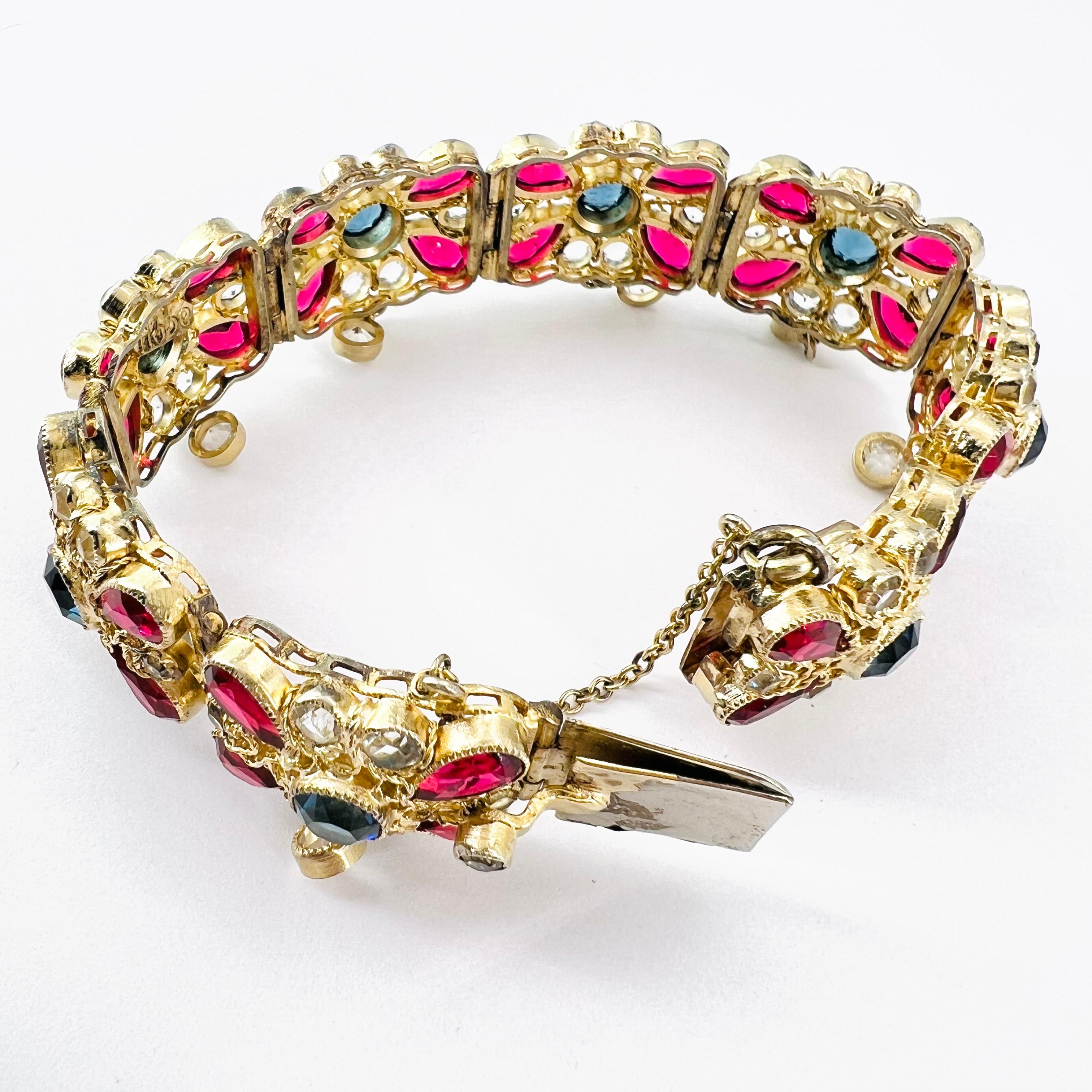 Elaborate Signed Hobe bracelet from the 1930s with ruby, montana blue and clear open back crystals set into an intricate filigreed frame each panel has a single clear bezel set crystal dangle. Every stone is bezel set and embellished with looped