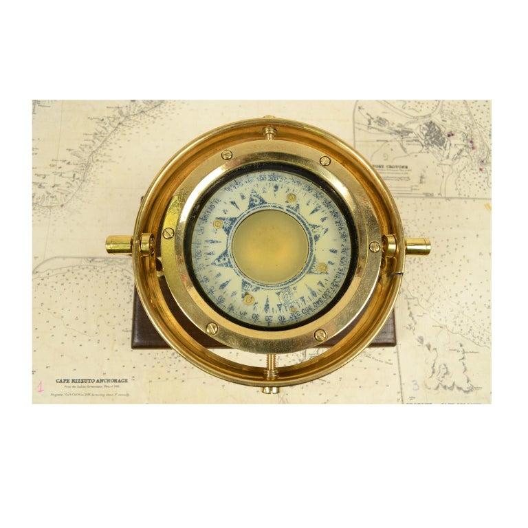Nautical liquid compass, brass, on universal joint signed Kezar India made in the 1930s mounted on a walnut board. The compass is made up of a cylindrical brass container, on the bottom of which a stem of hard metal is fixed, on which the compass
