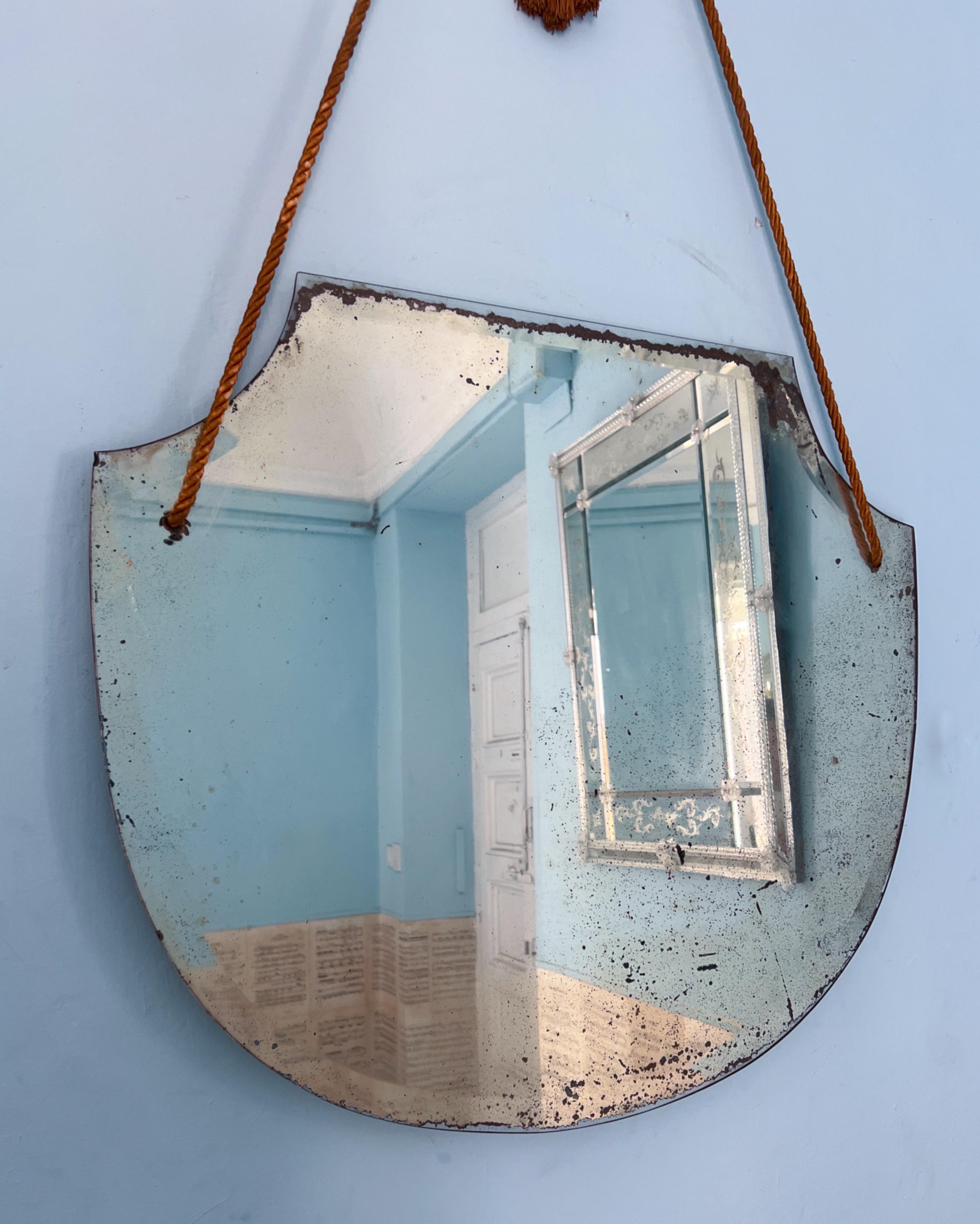Questo affascinante specchio da parete degli anni '30 vanta una bellissima e intricata patina sul vetro, che ne esalta il fascino vintage. Conserva il nastro originale per essere appeso, presentato in un bel colore marrone caramello. Si prega di