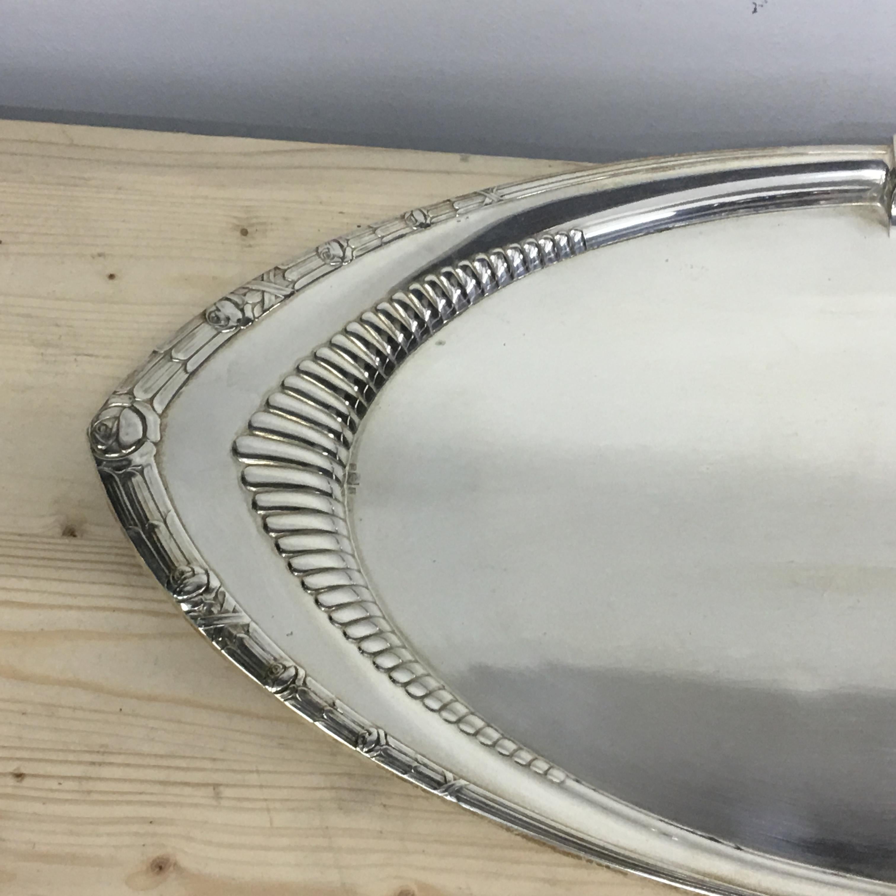 Graceful and elegant Art Deco oval tray in silver plate. The border is printed with a light geometric decoration interspersed with delicate stylized roses. The part between the border and the top of the tray is embellished with fine embossed fluted
