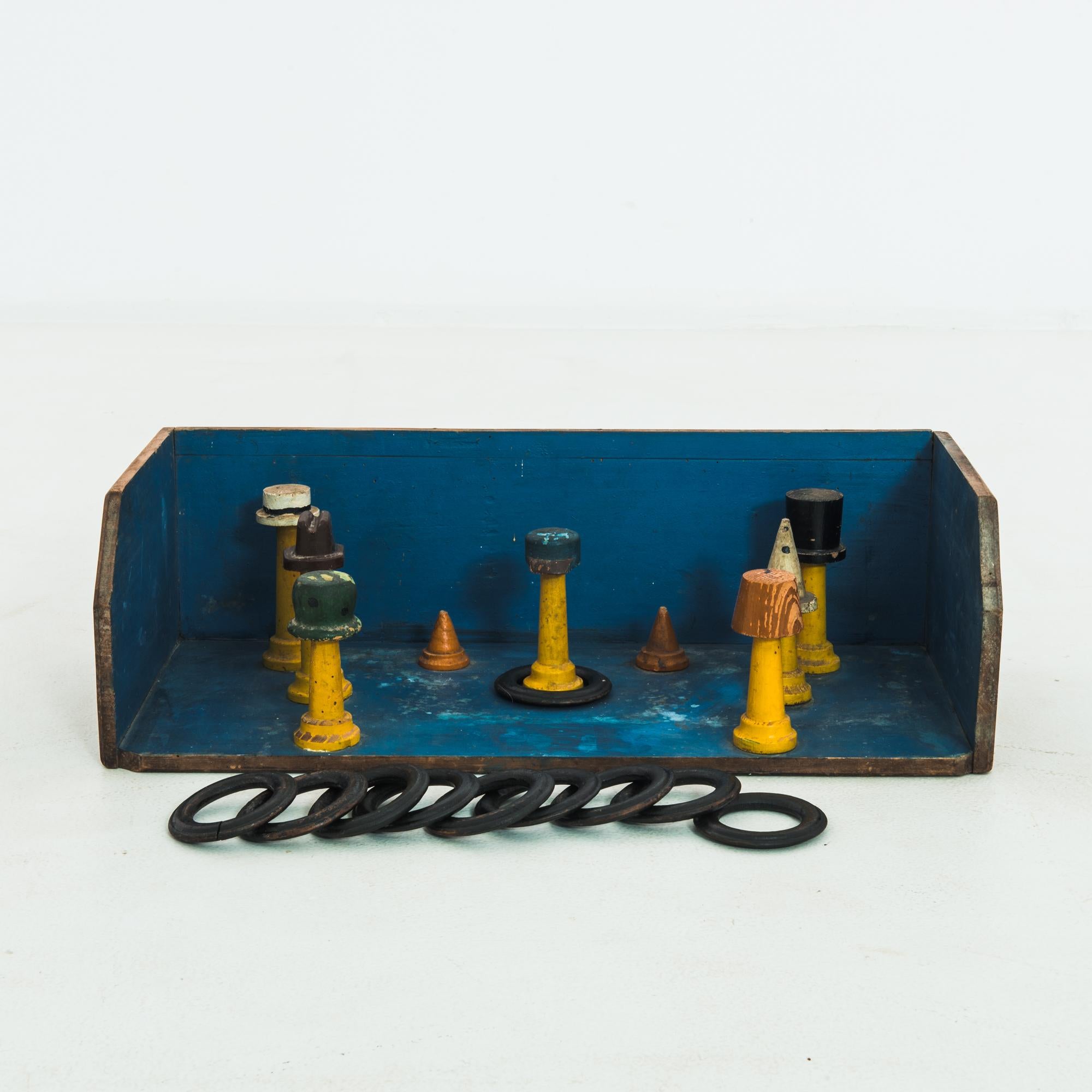 Made in Belgium, circa 1930, this wooden ring toss game will inject color and a whimsical spirit into any space. The yellow wooden posts are topped with caps of different shades and displayed against a blue backdrop. Ten black rings are included in
