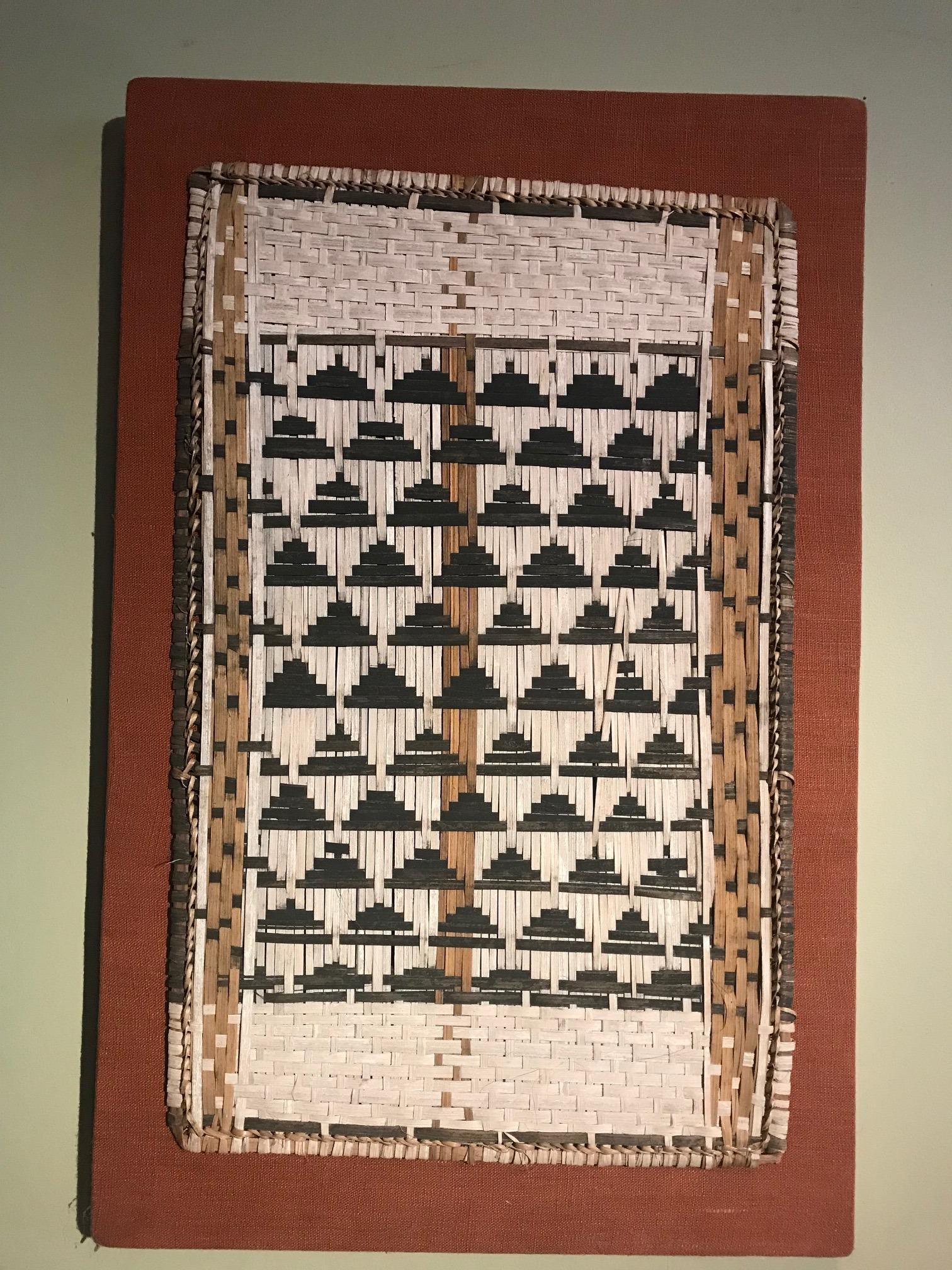 Este panel de 1930, procedente de la cultura mbole de la República Democrática del Congo, ha sido tejido con fibra de corteza. Se han utilizado hebras de fibra de color oscuro, teñidas con las raíces de un platanero, para crear atrevidos y
