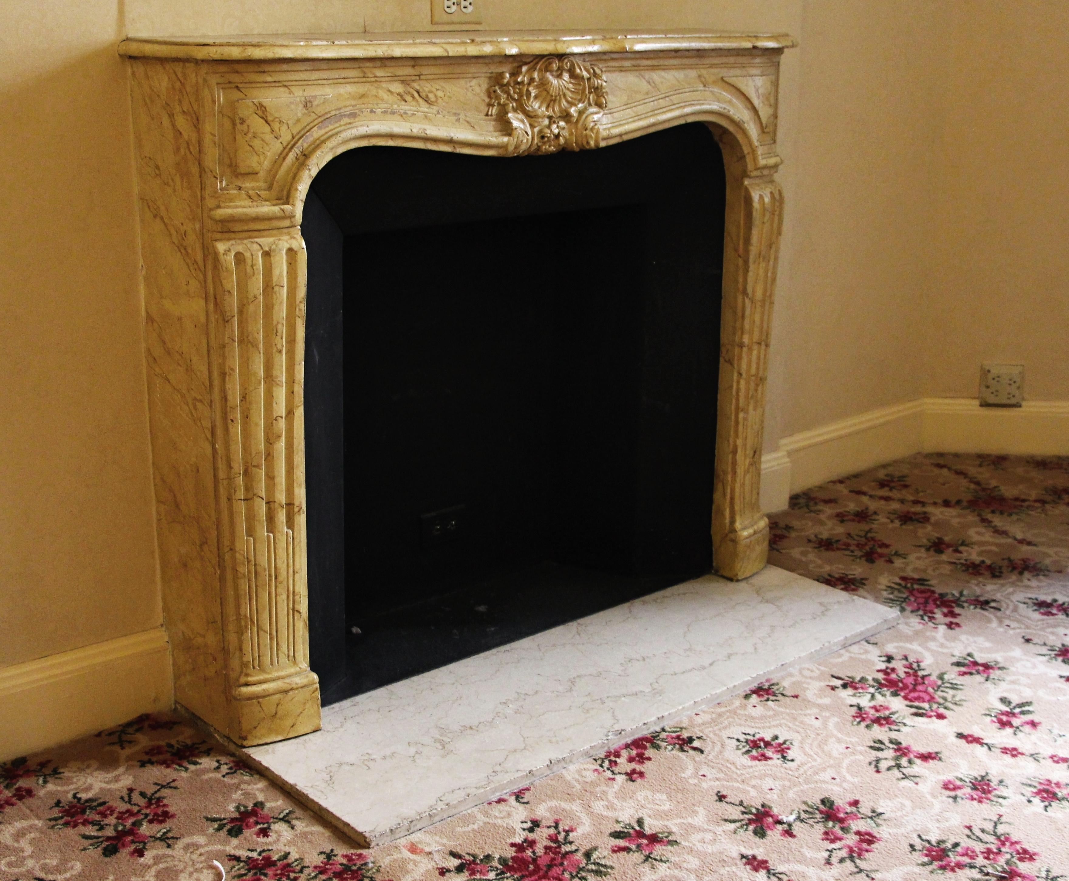 Louis XV carved limestone mantel with faux Sienna marble finish and Crema Marfil marble hearth. Made in France. This mantel was one of a group of antique mantels imported from Europe and installed in the Waldorf Astoria hotel in the 1930's when the