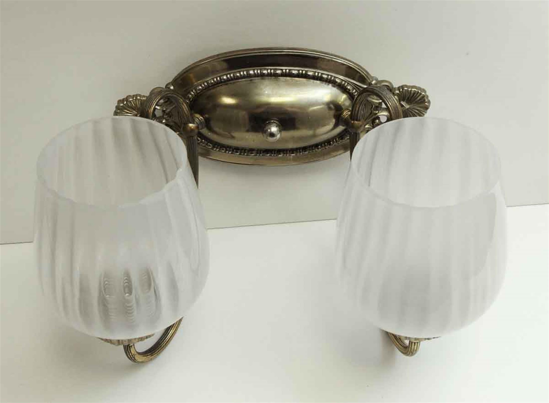 20th century two-arm silvered cast brass sconce with foliage detail and two Italian glass shades. These sconces adorned various bathrooms of the towers of the NYC Waldorf Astoria Hotel when it opened in 1931. The arms of the sconces are brass with a