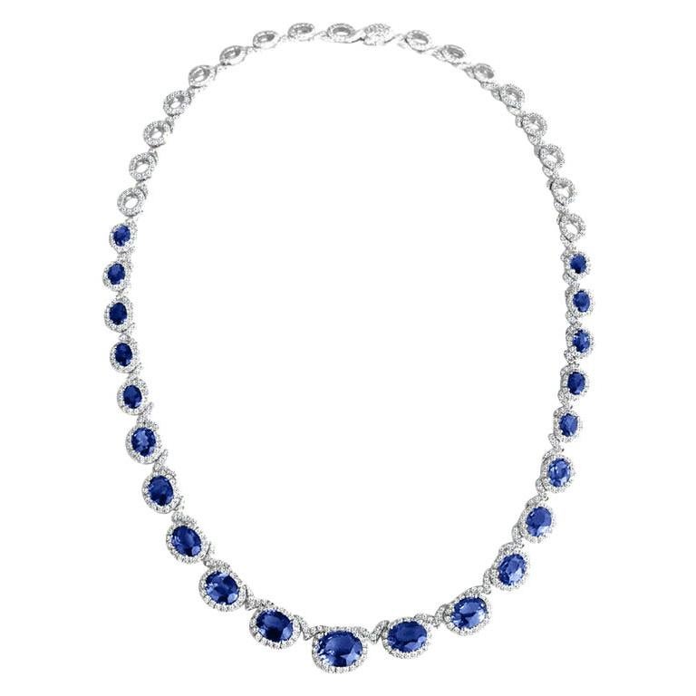 This necklace features 21 oval cut vivid blue sapphires in a graduated pattern, each in a halo of round  natural white diamonds, spanning three-quarters of the necklace length. Additional natural white diamonds alternate with each link.
The back
