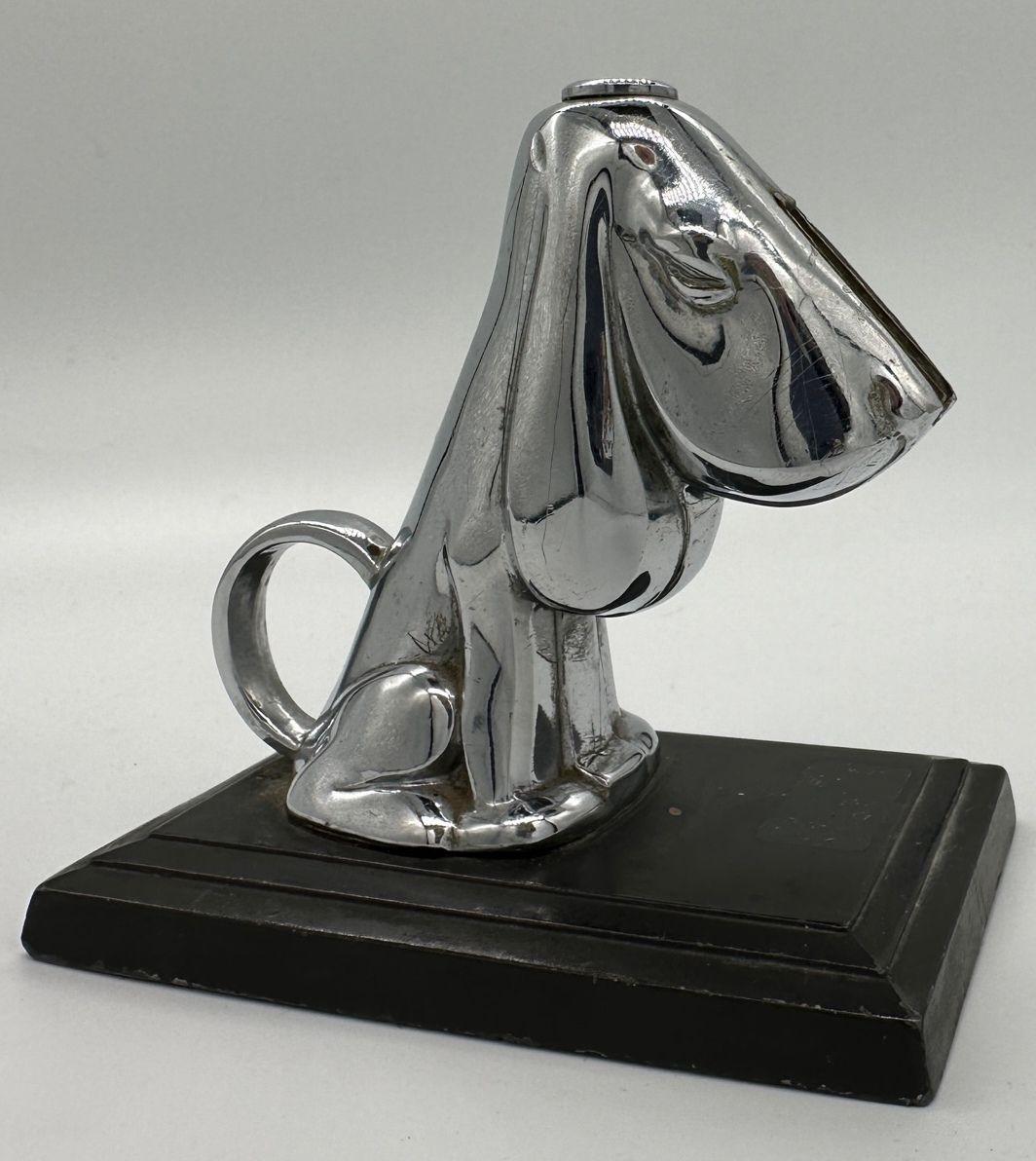 In 1935, a desk-mounted striker lighter was crafted. It featured a basset hound canine adorned with a layer of chromium plate, positioned on a sleek black enameled metal base. The tail of the hound was ingeniously shaped into a small handle. This