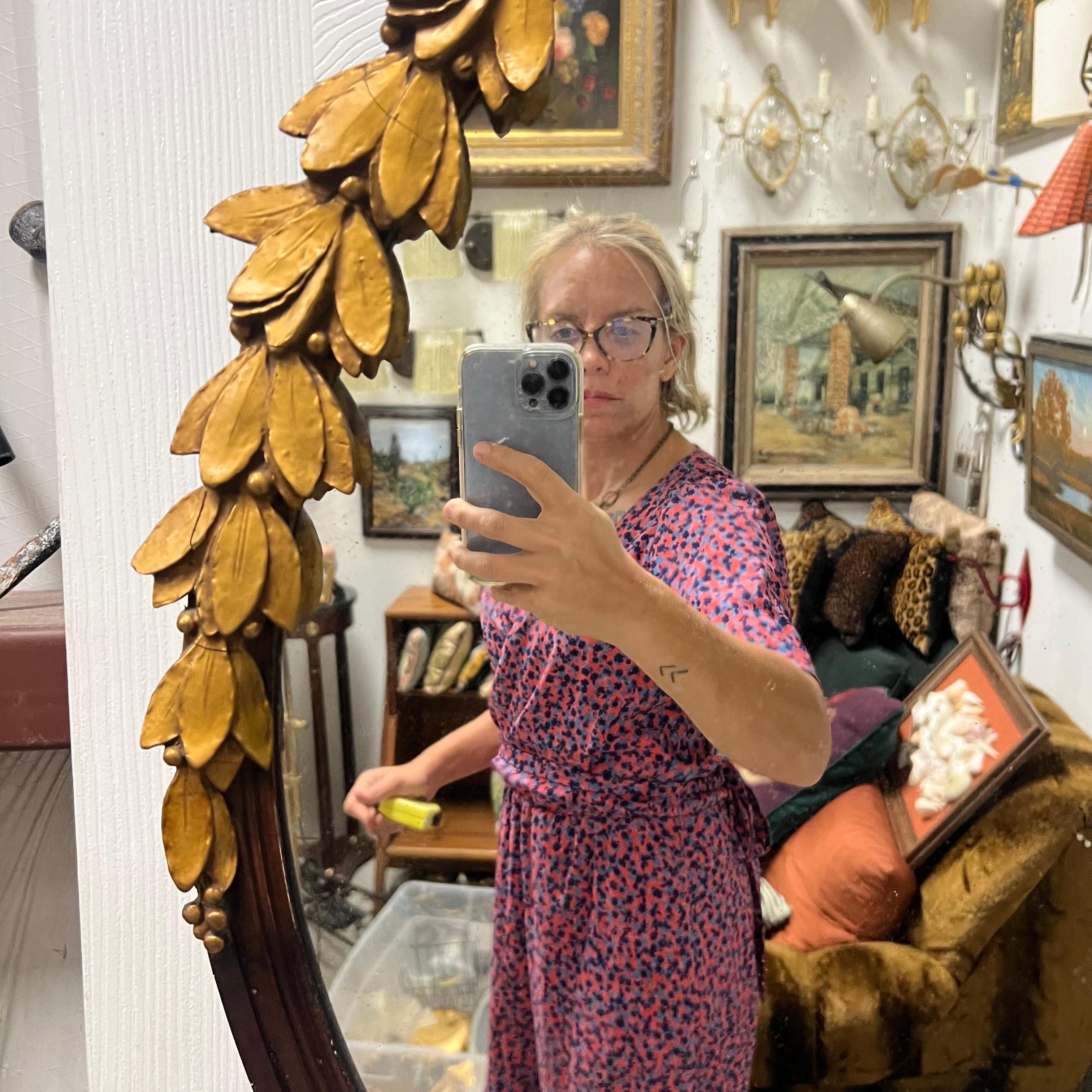Carved gilt wood round mirror with leaves and a bow adorning the top half.  The mirror is marked on the back “July 1936 metropolitan mirror and glass co.”