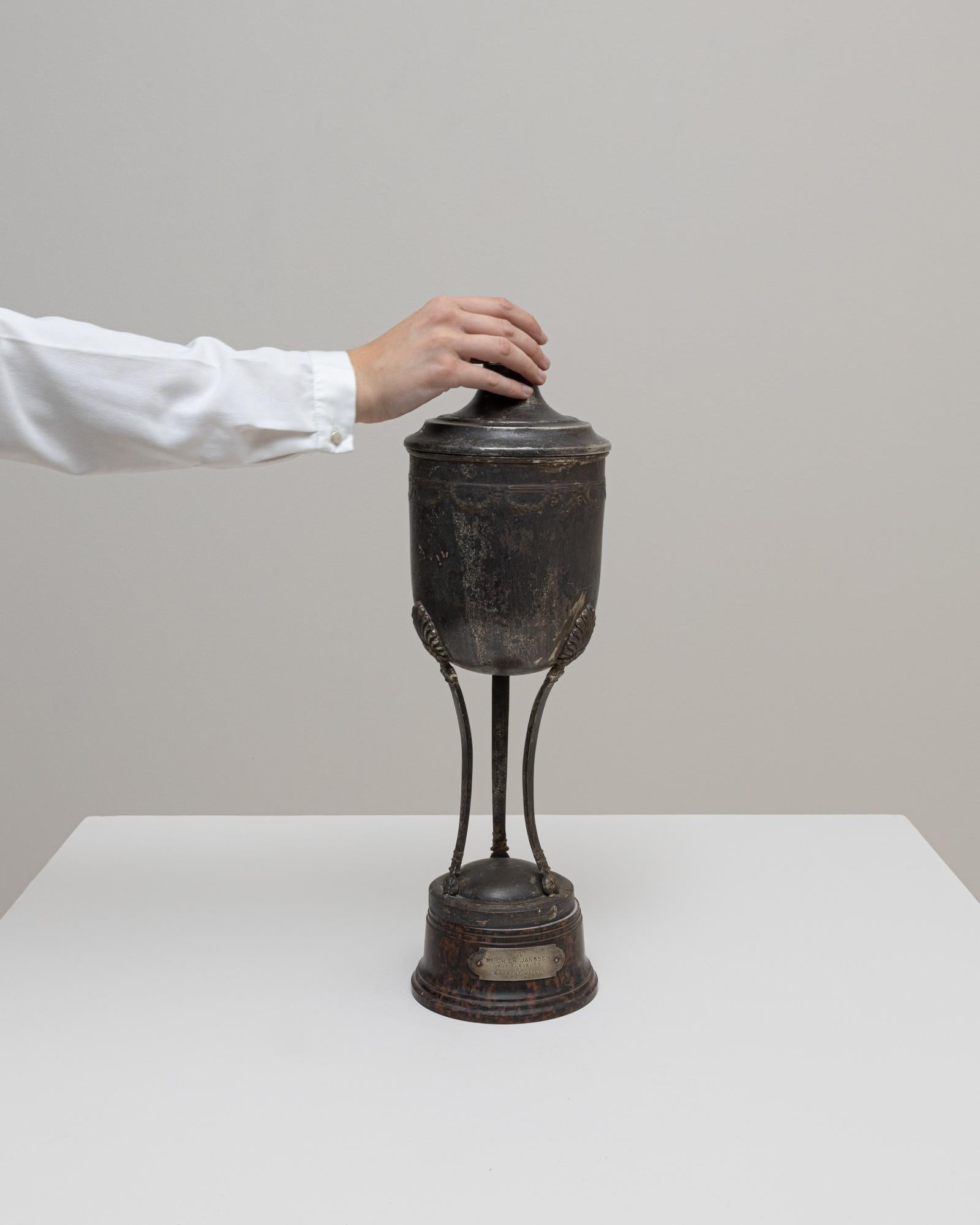 Questo calice belga placcato in argento del 1937 presenta una forma elegante e scultorea elevata su tre sottili supporti sopra una base di legno arrotondata con la sua targa di presentazione originale. La coppa con coperchio presenta una silhouette