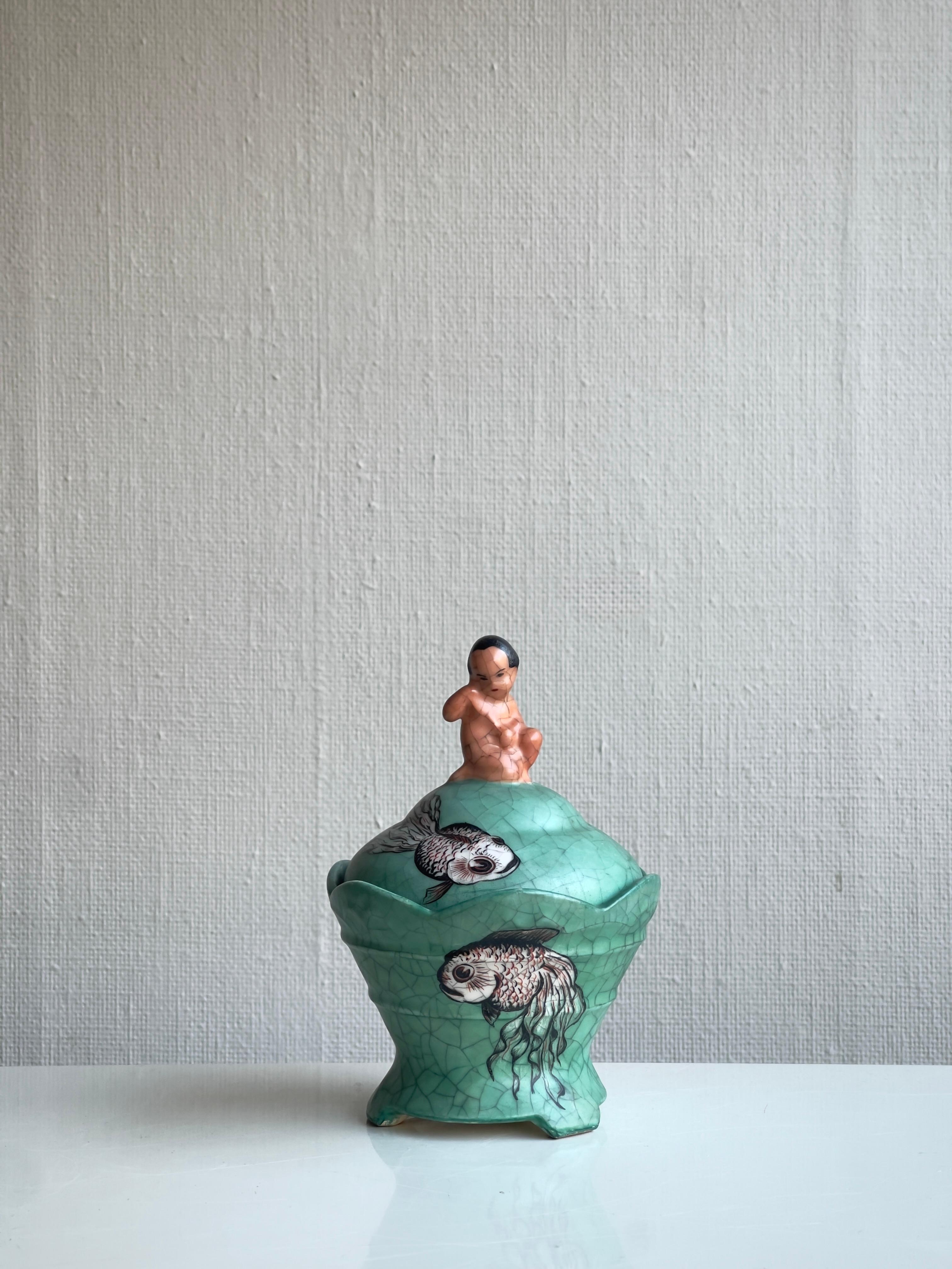 Eine seltene, ausdrucksstarke dänische Keramikschale mit Deckel von 1937, die sich durch ihre leuchtend türkisgrüne Craquelé-Glasur auszeichnet und mit außergewöhnlicher Sensibilität handbemalt wurde. Der Deckel wird von der Skulptur eines Jungen