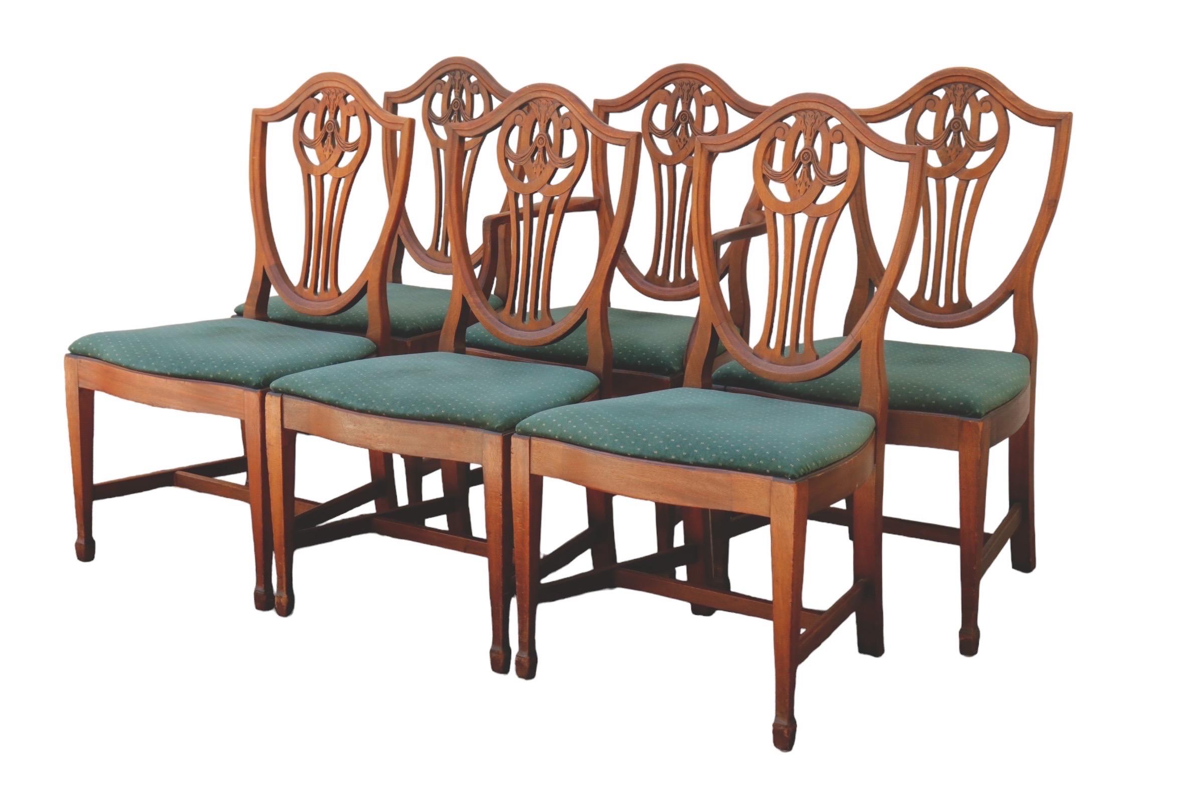 A set of six shield back dining chairs (five side chairs and one armchair) made in the 1930’s by Macy’s of New York. Shield shaped seat backs are beveled, with a pierced back splat simply carved with scrolls and swag details. Trapezoid shaped seats