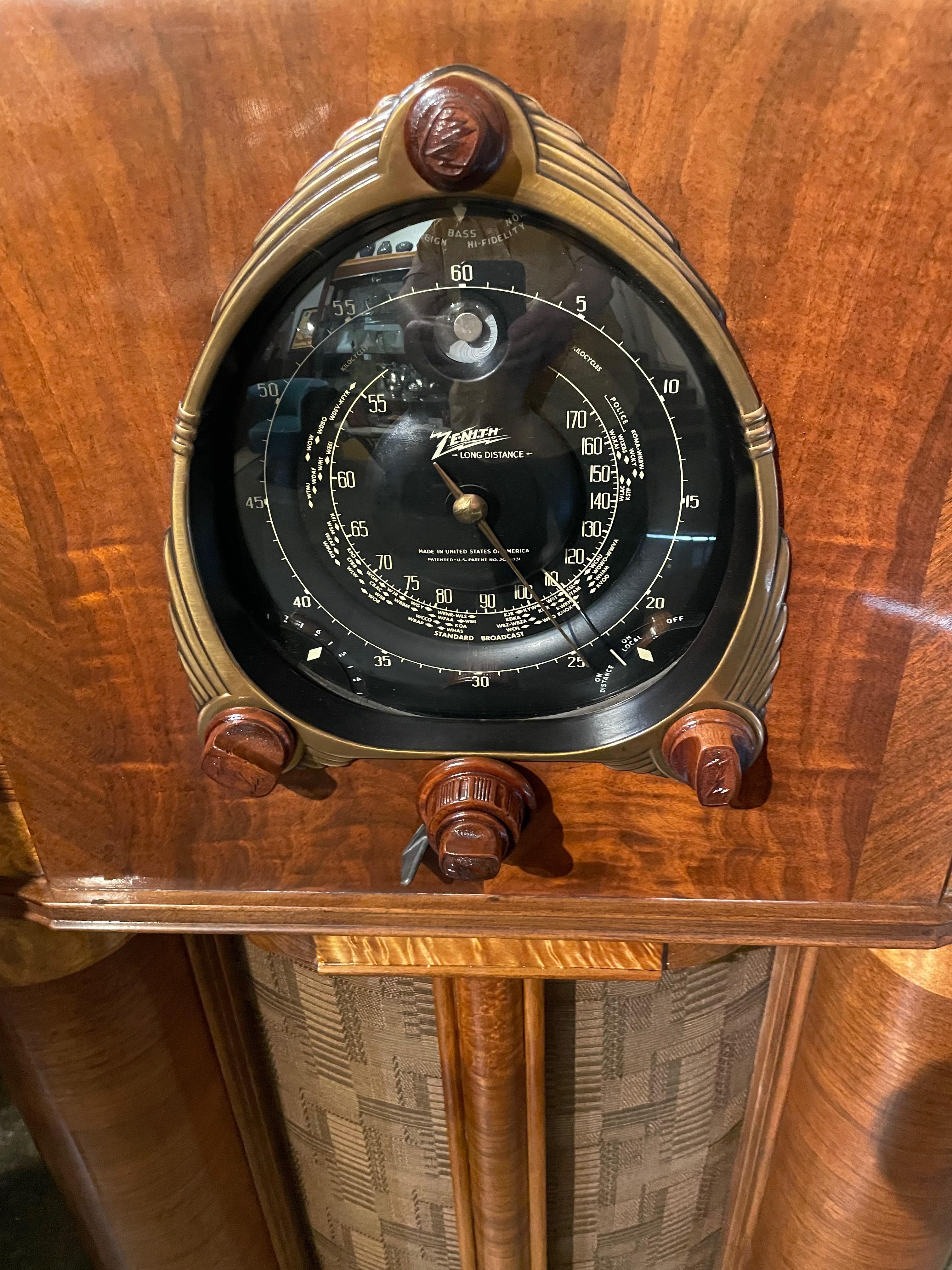 This is a 1938 Zenith 12 tube model 12S265, Zenith’s most famous and collectible year. It is sporting the fabulous “Motor Drive Robot Shutter Dial” and green tuning eye. The large black dial is in very nice shape. The cabinets’ book-matched walnut