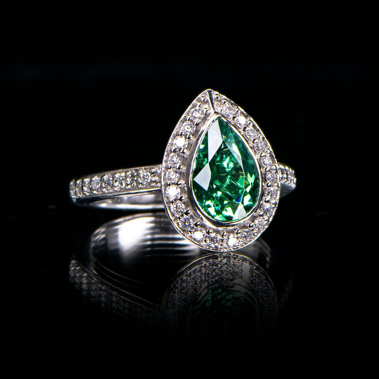 This handcrafted vintage style ring features a 1.94 carat pear cut green Tourmaline in a grain set cluster (halo) setting. The setting is elegantly flanked with a grain set diamond band. The total diamond weight is 0.38 carat (Colour F, Clarity VS).