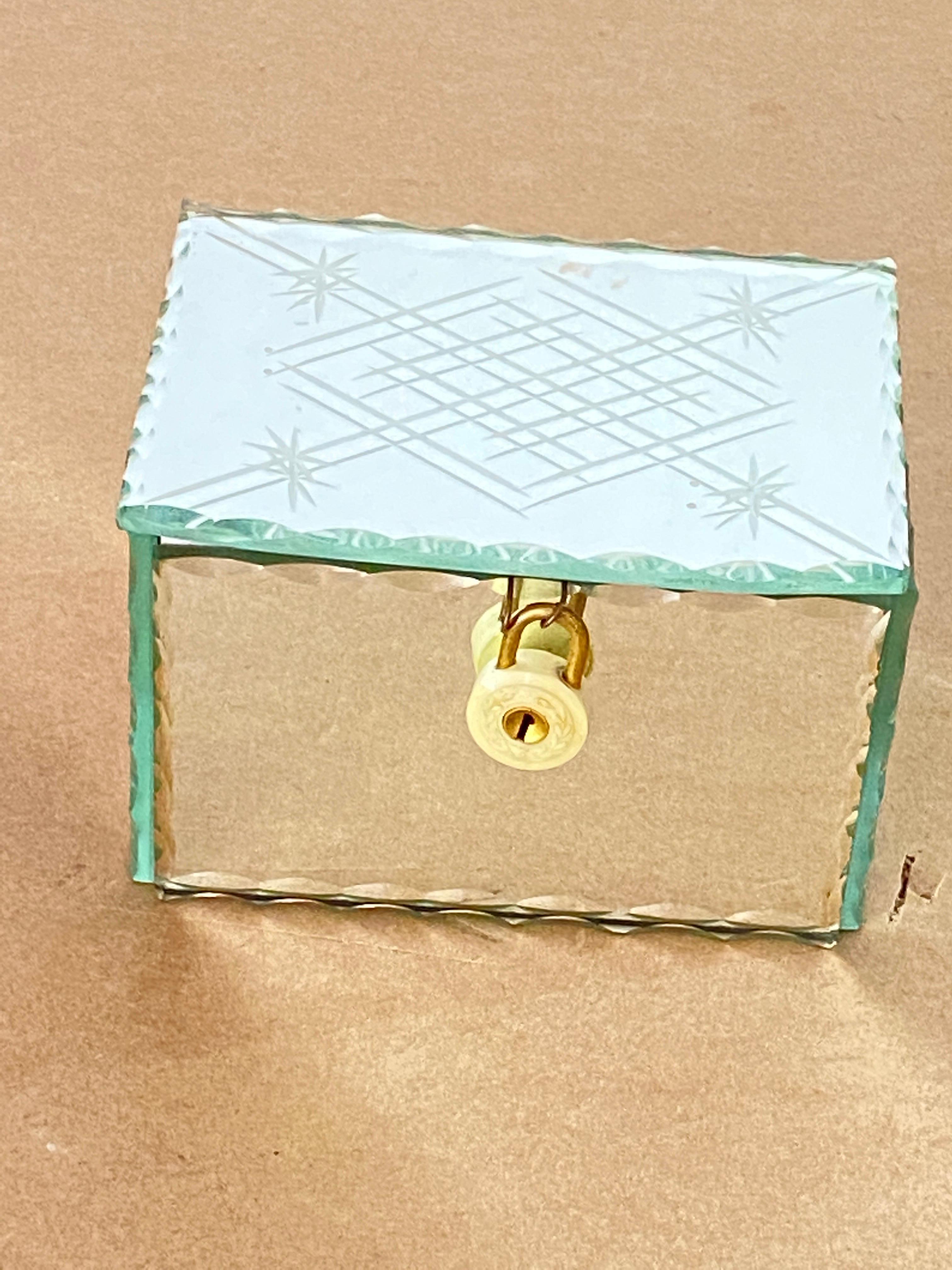 It is a rectangular beveled glass box.
It is closed by a padlock, which is rather decorative.
This box was made in France during the 1940s. It is a jewelry box, which is also a decorative box.