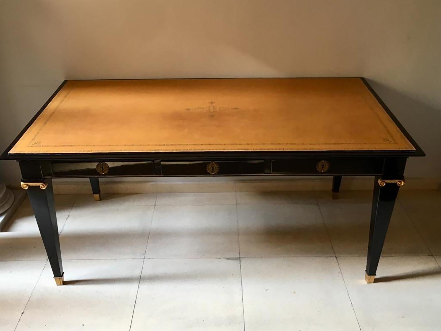 French desk table in Andre Arbus style, black lacquered wood, with jonic gold bronzes and sabot-finished legs, three drawers and leather cover with gold filigree.