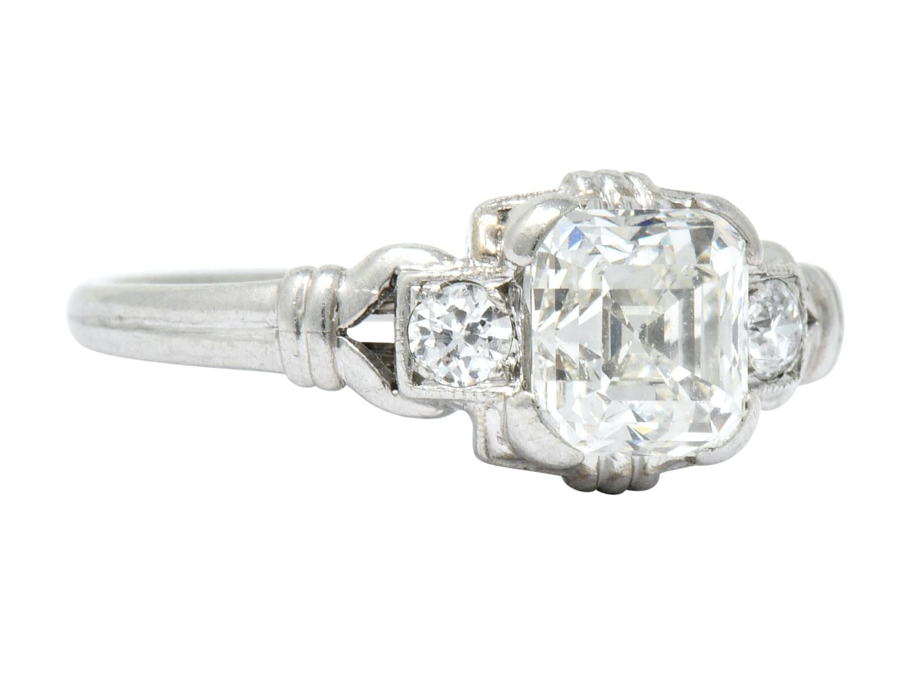 Centering in a low profile square form head, with an asscher cut diamond weighing approximately 1.25 carats, J color and SI1 clarity

Flanked by two transitional cut diamonds weighing approximately 0.10 carat total, J color and SI clarity

Completed