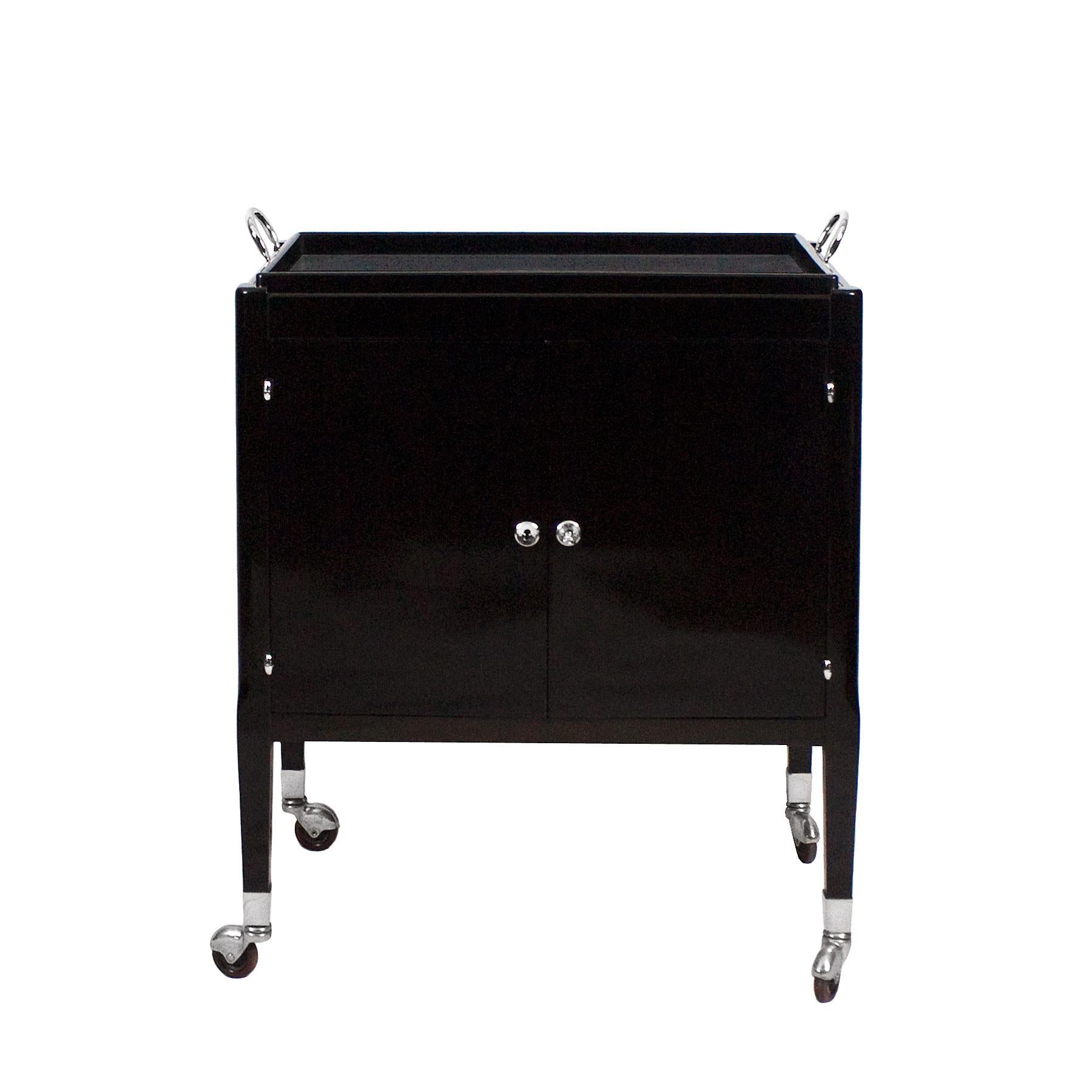 Dry bar on wheels, dark stained and French polished mahogany, two doors. Interior with light wood, two compartments, one with two sliding plates and one drawer and the other for bottles and napkins rack. Removable tray on top. Nickel-plated brass