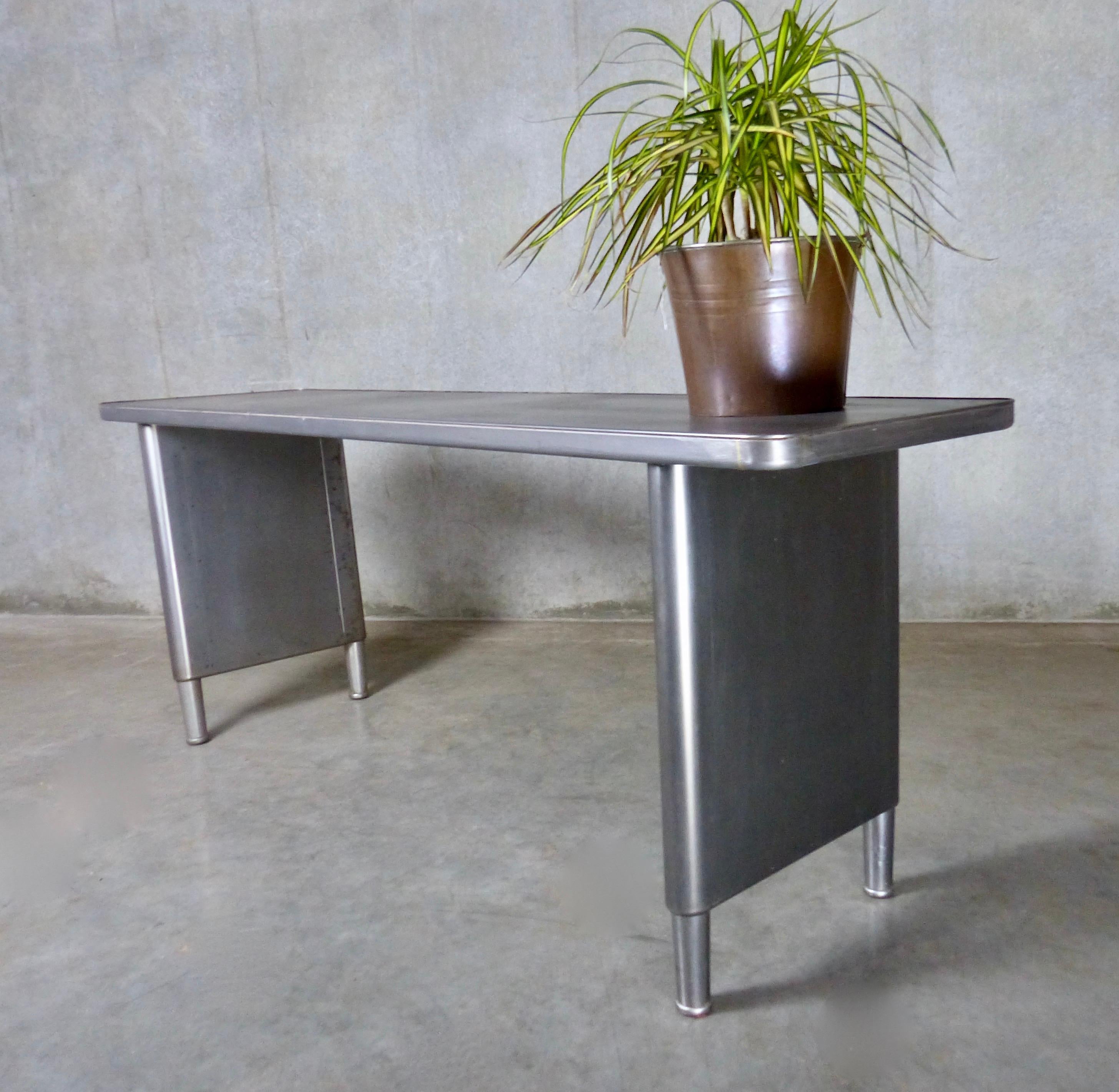 A raw metal office/work table from circa 1940 that makes a great console, hall, or dining table. Panel steel legs can be moved toward the centre of the table to allow people to sit comfortably at its ends. Great piece of industrial design that’s