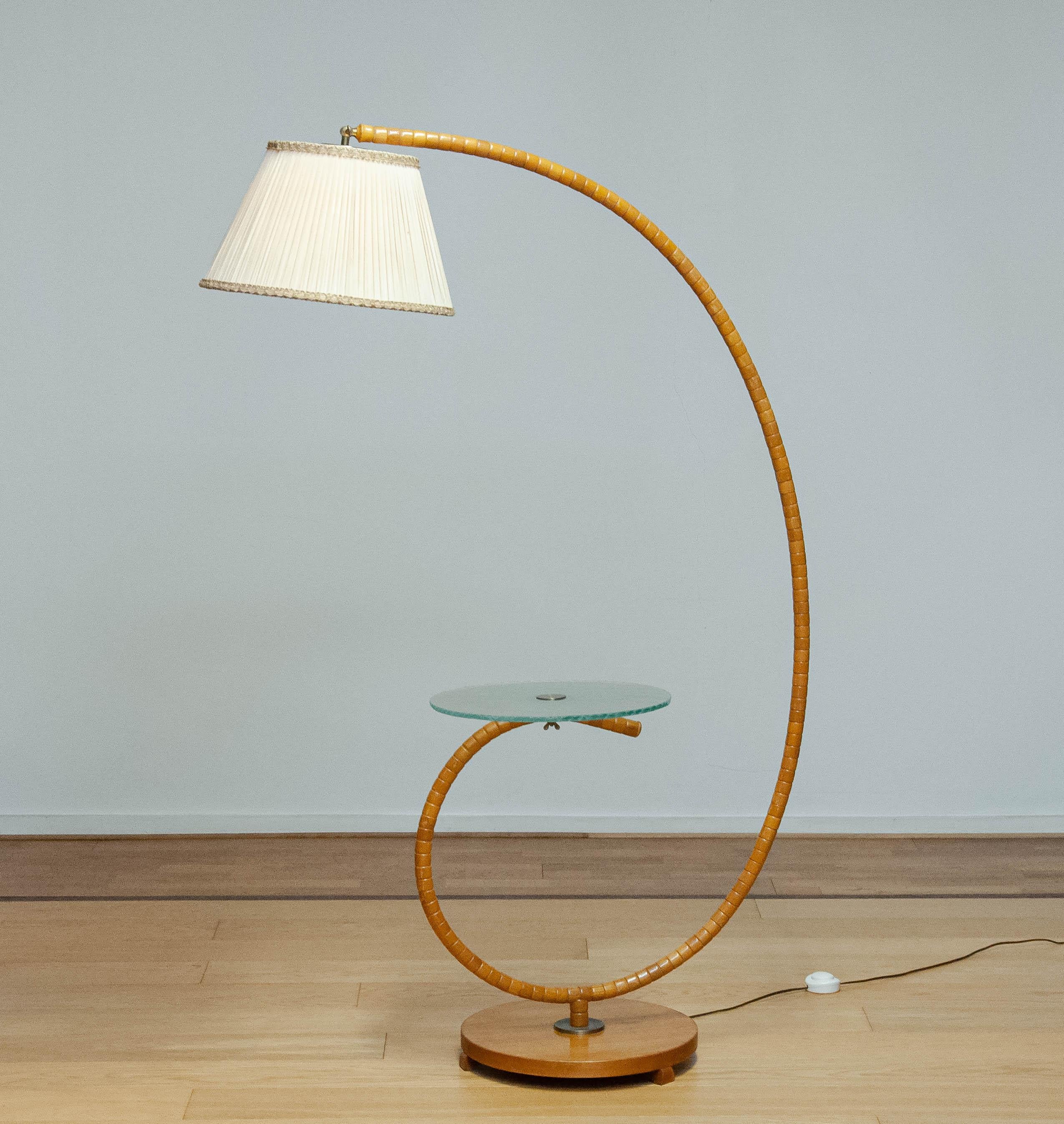 Absolument magnifique et très rare lampadaire Art Nouveau fabriqué dans les années 1940 en Suède par IWO à Mariestad.
La lampe est fabriquée en bois d'orme et est combinée à une table en verre d'art. La table en verre d'art 
La partie supérieure