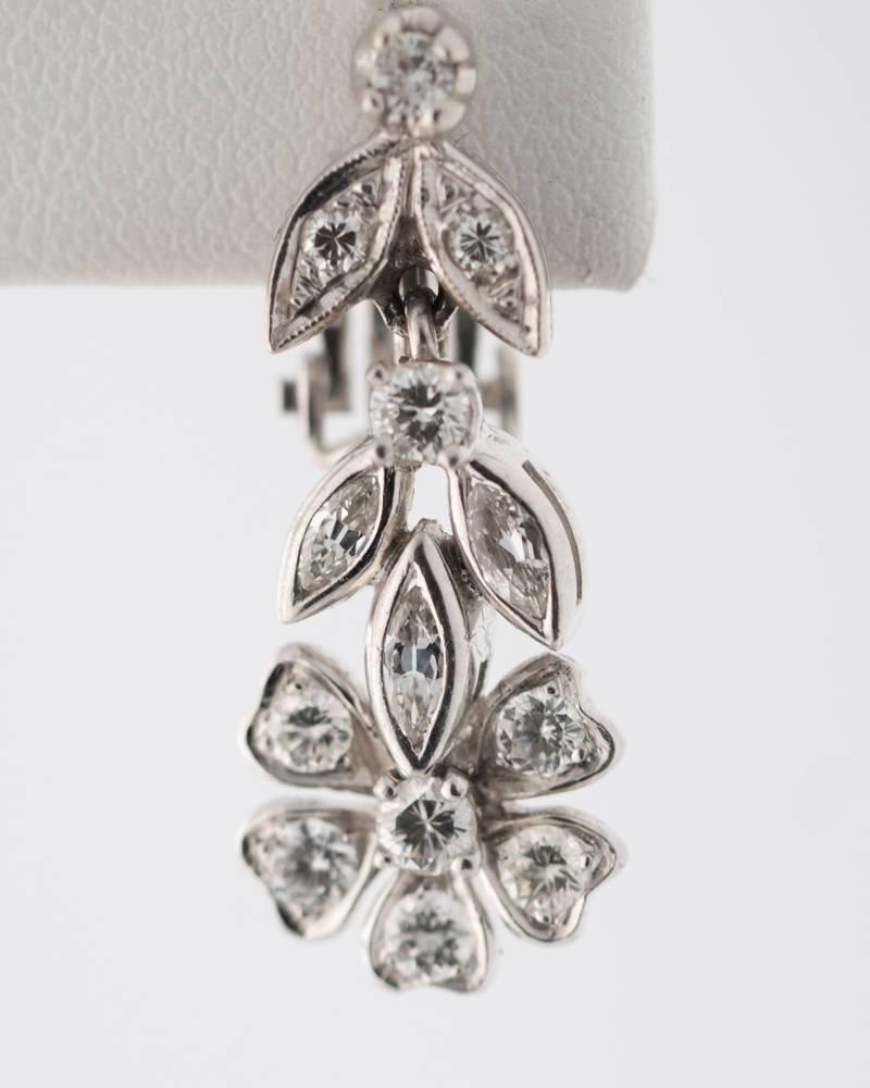 These 1940s 1.0 carat total weight and 14 karat white gold flower motif dangle earrings feature bezel set European cut Marquise and screw prong set Transitional cut diamonds. They have hinged clip on French back posts and measure 28 millimeters long