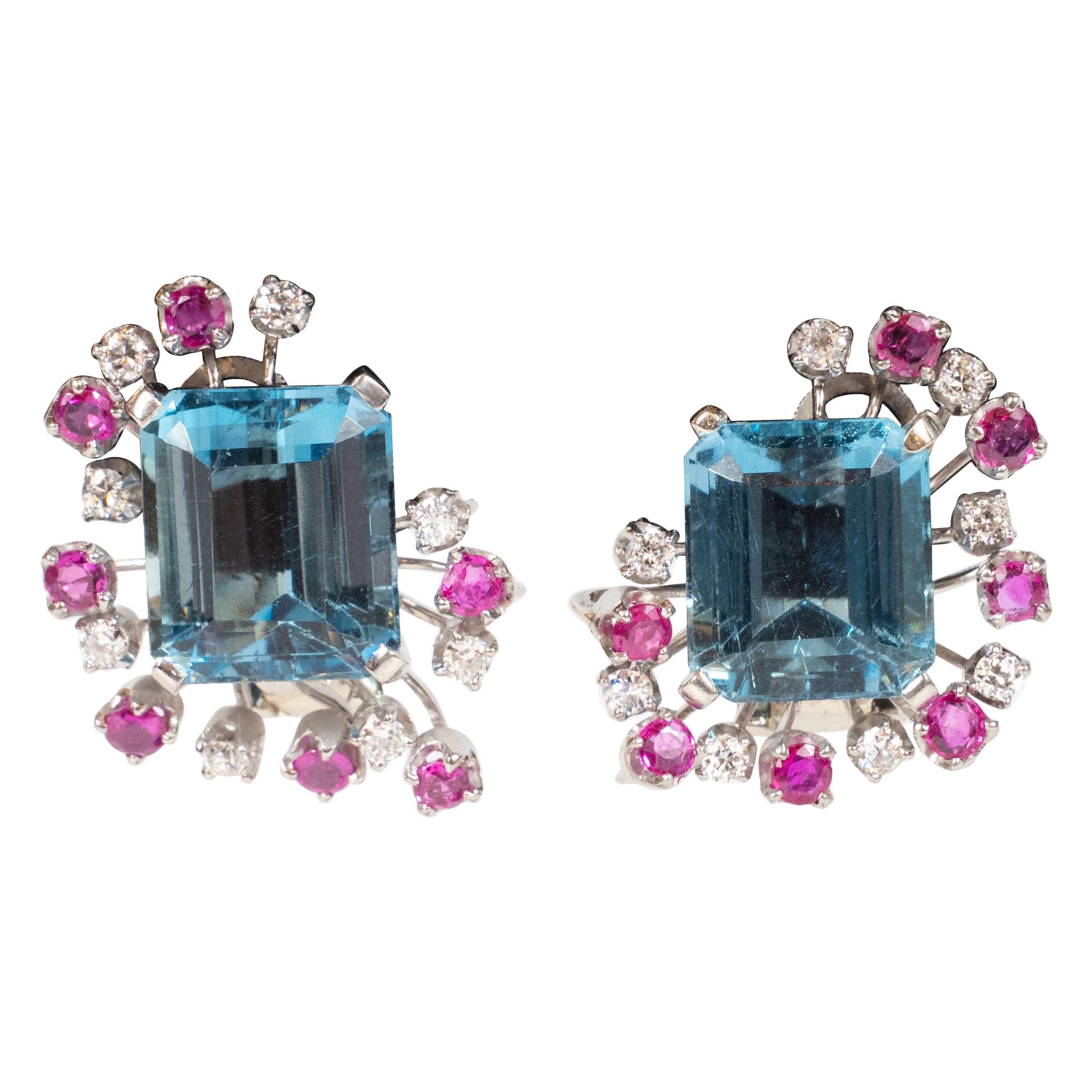 This stunning pair of retro earrings were realized in the United States, circa 1940. They offer 12 carats of aquamarine (6ct in each), surrounded by a cluster of alternating rubies and diamonds, all set in platinum. Additionally, they have 1.45
