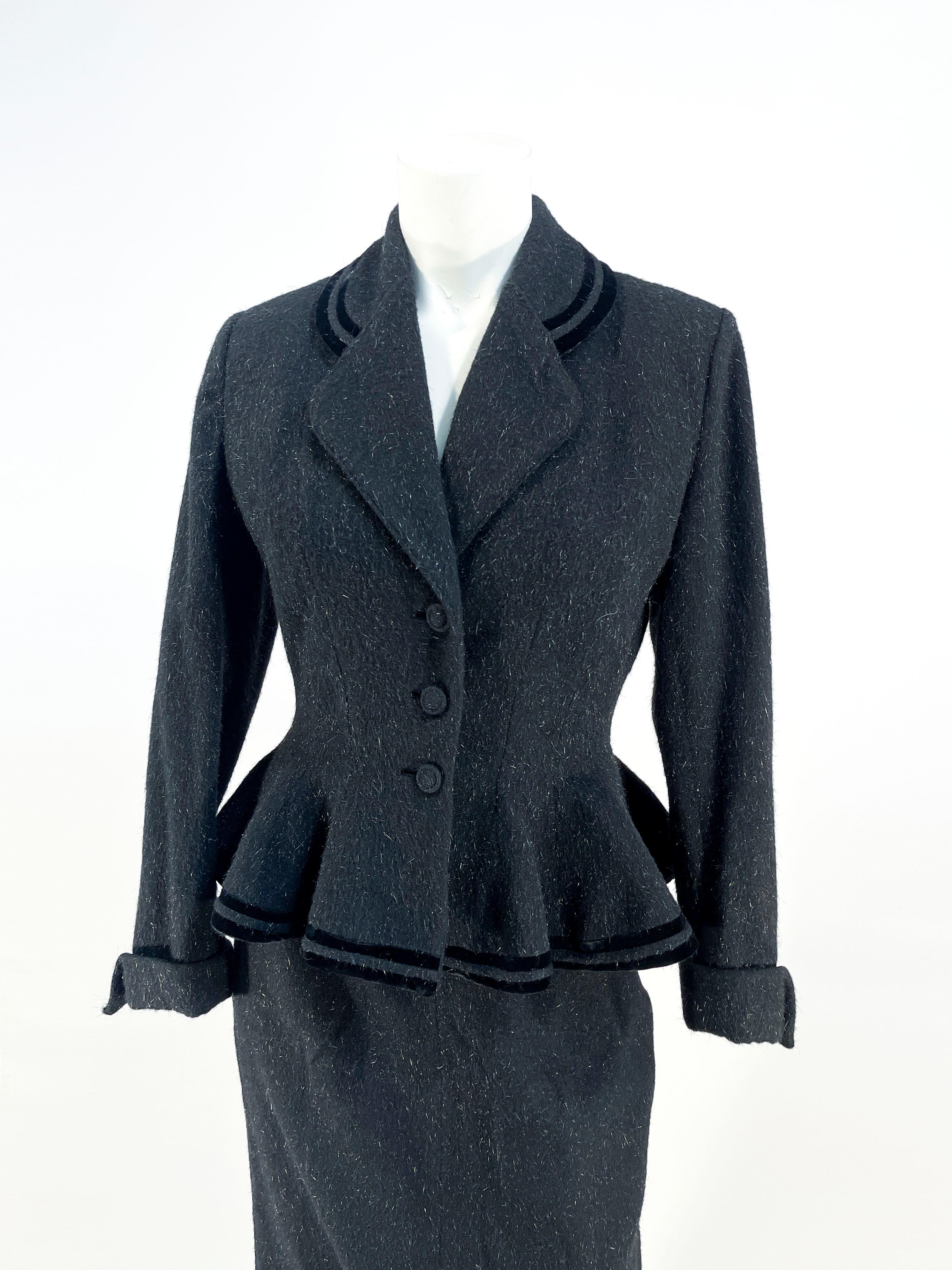 Late 1940s to early 1950s Black Lilli Ann flecked wool jacket and skirt suit. The jacket features a notch collar, covered designer buttons, in-set button holes, double bands of velvet trim accenting the color and hem, and a fitted wasp waist that