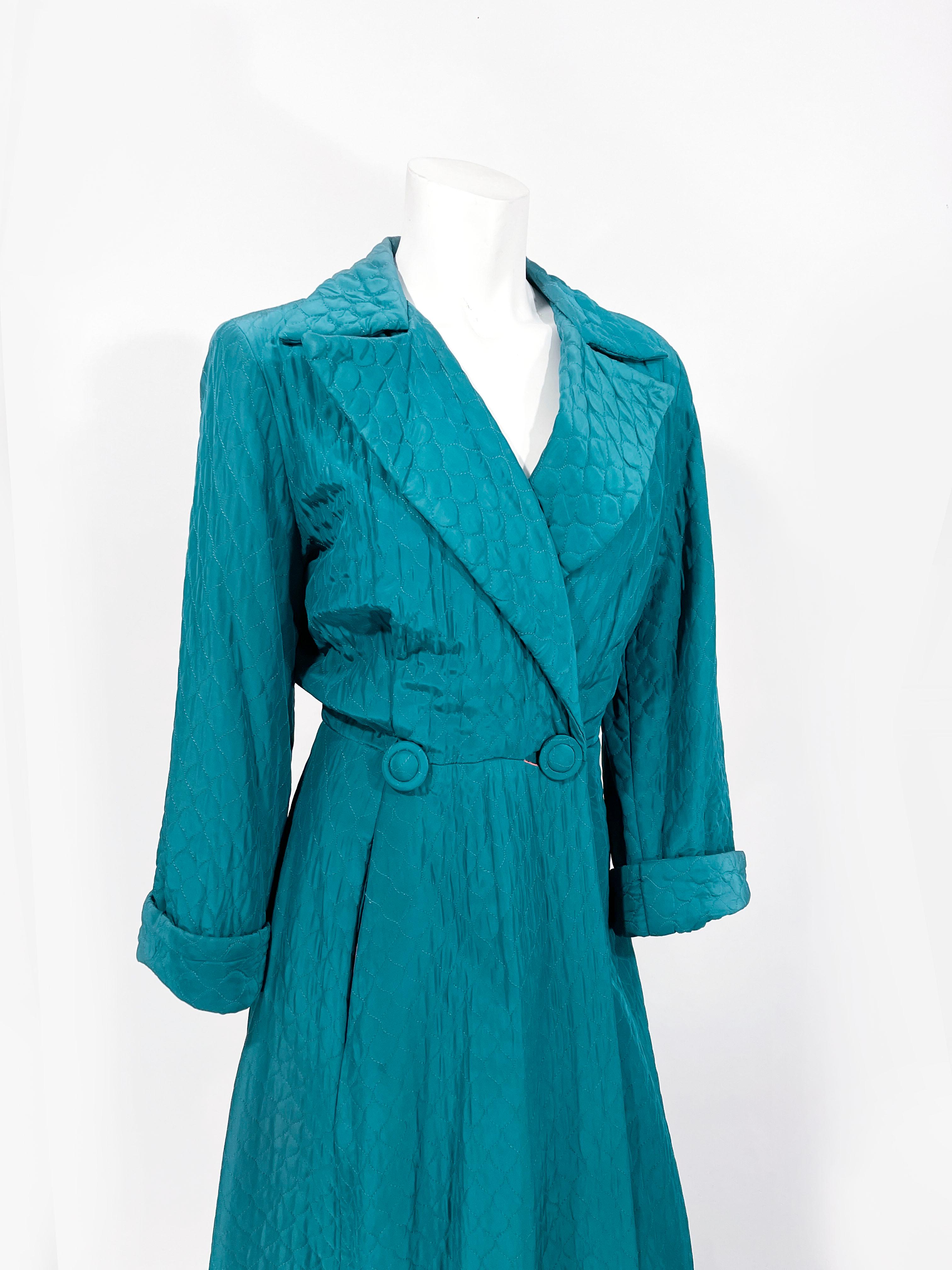 Late 1940s to early 1950s dark teal green quilted house robe/coat featuring a double button closure with designer covered buttons, a wide peak lapel, rolled and cuffed full length sleeves. The interior is fully lined with a rose salmon colored