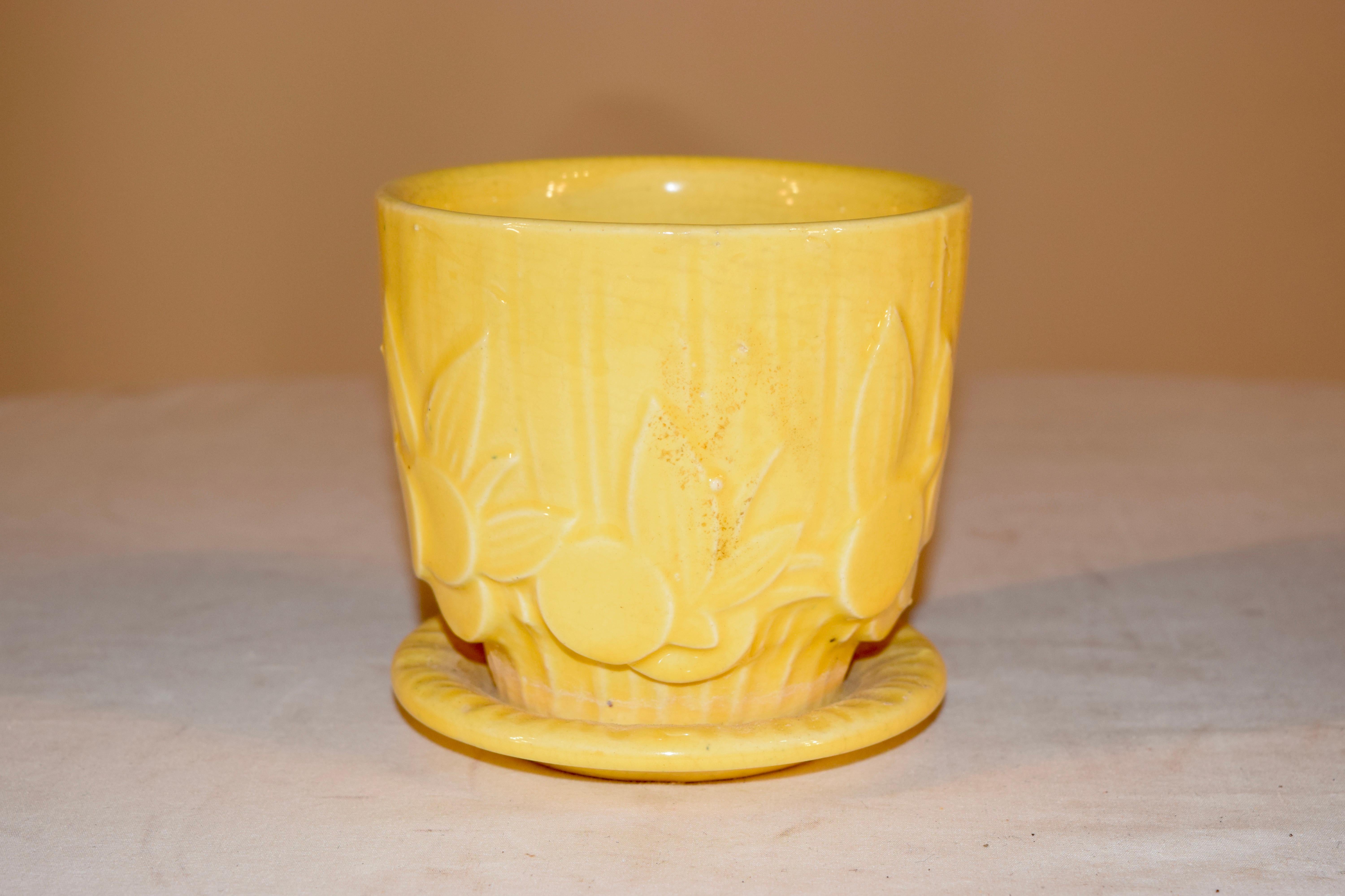 1940s American small flower pot with attached saucer. The flower pot has a sweet molded pattern with fruit and leaves on it, and there is a drain in the bottom of the pot.