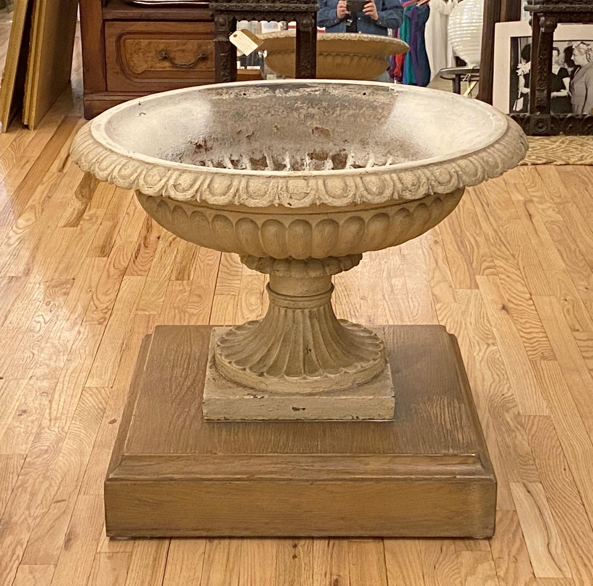 Retrieved from a Manhattan backyard garden, this 1940s antique cast iron urn or planter rests on a removable custom made wood platform. The planter features an egg and dart trim around the rim the fluted bowl has a drain hole. Original patina.