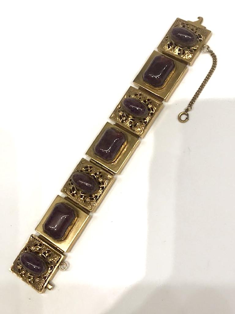 A stunning  and substantial post war 1940s bracelet with purple glass cabochons. Most likely West German. Original soft gold patina. Glass cabochons made with inclusions to simulate authentic stones. Each of the seven links is 1 inch square, set