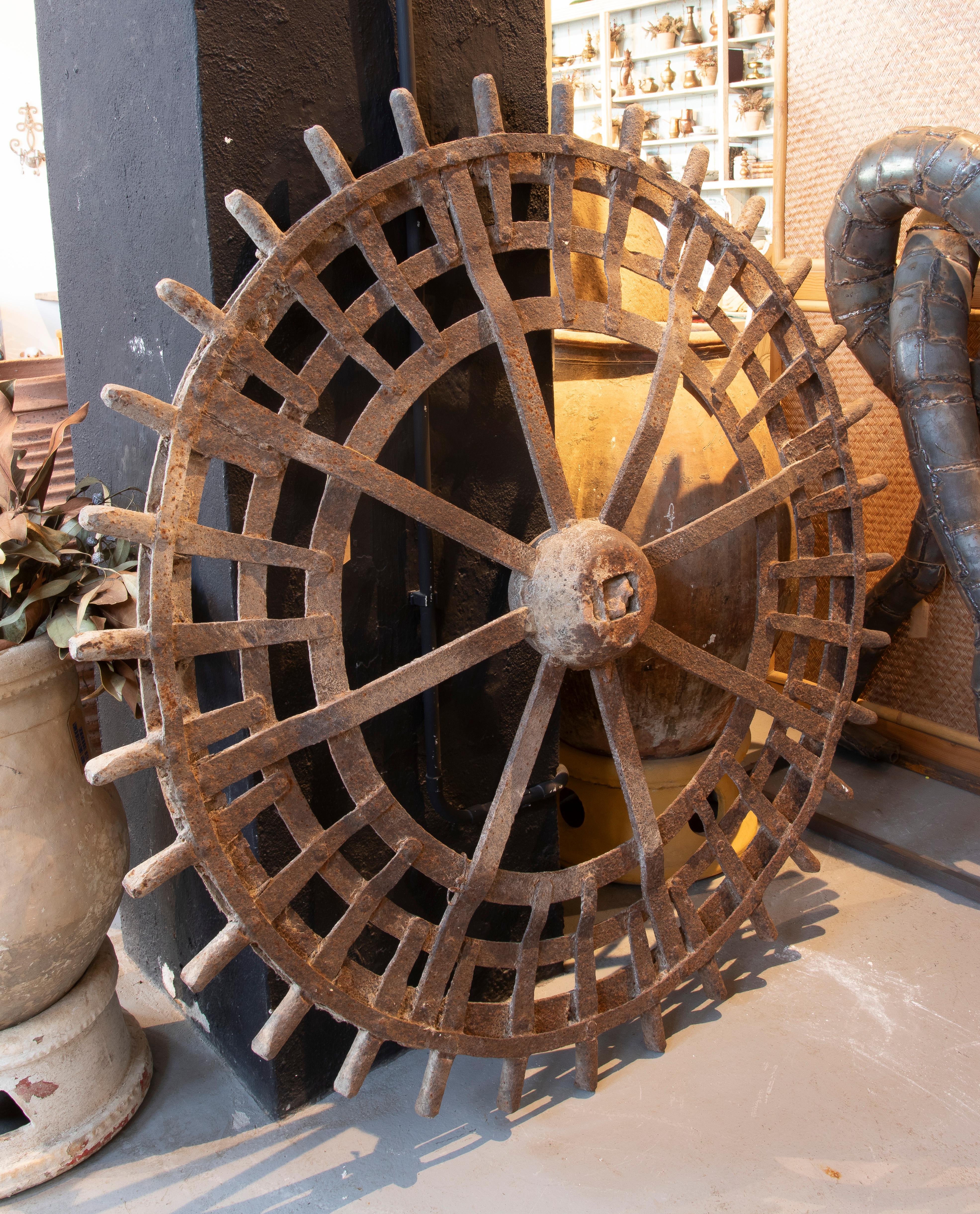 Impressive antique industrial wheel made of cast iron, notable for its intricate curved spoke design and reinforced structure. Originally used in agricultural or hydraulic machinery, this piece has been preserved with an attractive natural rust