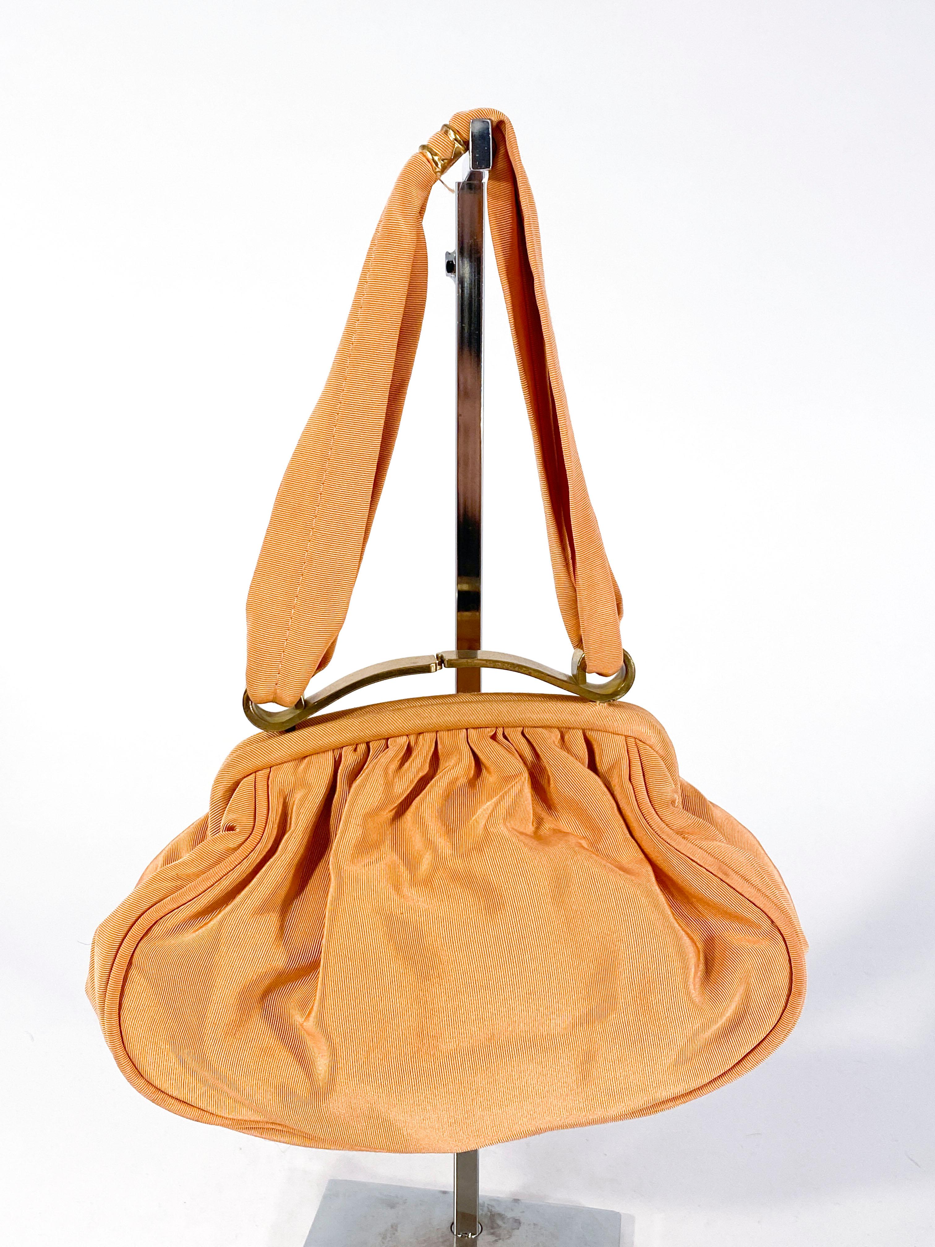 1940s twill hand bag in a rare tone of apricot twill. The closure is made of brass and designed into a decorative curse to match the decorative grip on the double sash handle. The interior is lined with an off-black twill and was an attached coin