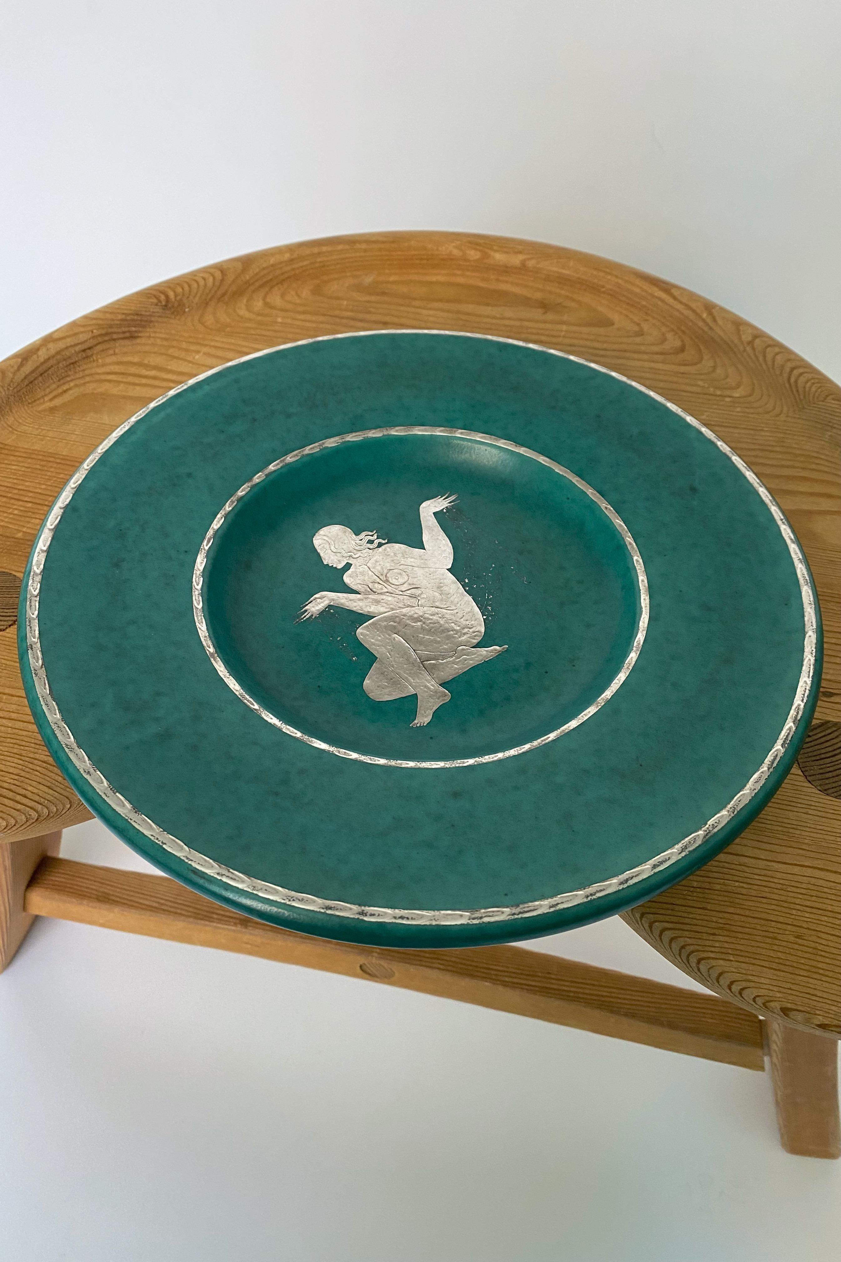 1940's Argenta stoneware plate with female siluett decor by Wilhelm Kåge for Gustavsberg. The now iconic Argenta stoneware collection with its green glaze and silver decorations is one of the most recognizable designs by Wilhelm Kåge. Designed in