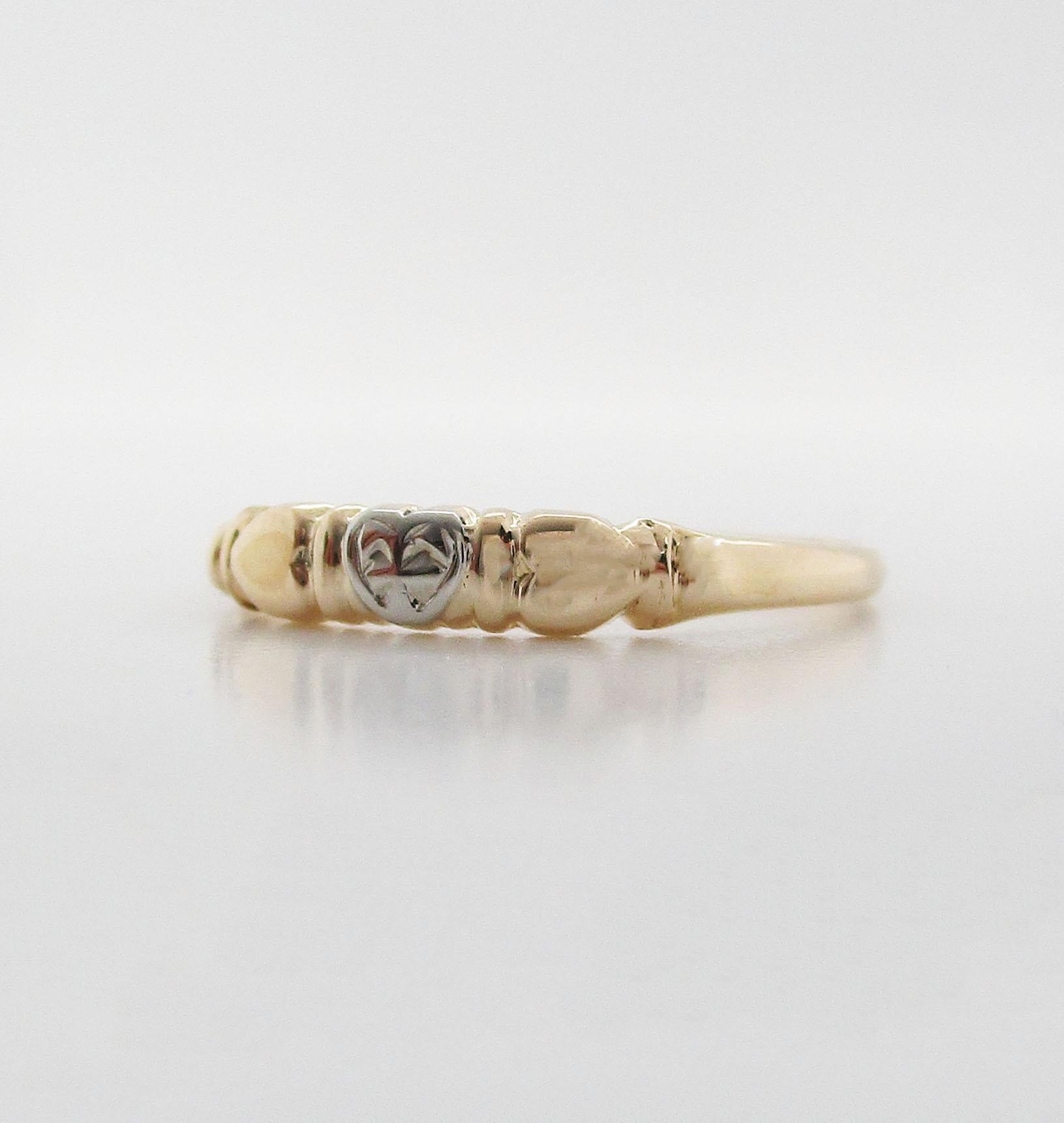 This is a lovely Art Deco Style band ring in 14k white and yellow gold. The ring features a subtle band design with a delicate heart center! The ring is in yellow gold and has two hearts on the shoulders pointing inward to a striking white gold