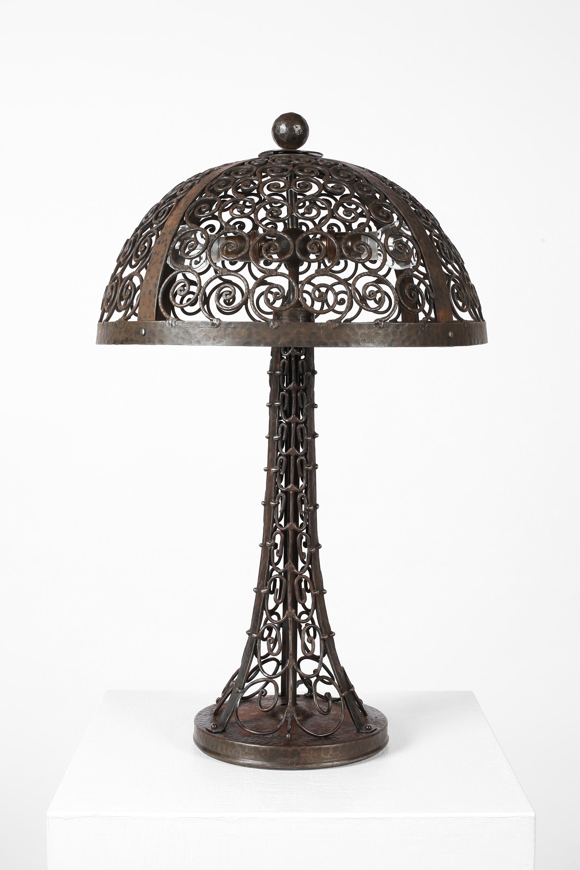 Grande lampe de table Art déco en fer forgé, battu et soudé. L'abat-jour en forme de dôme, avec son fleuron en forme de boule, repose sur une base effilée dont l'ensemble est orné de motifs en spirale complexes et ajourés.