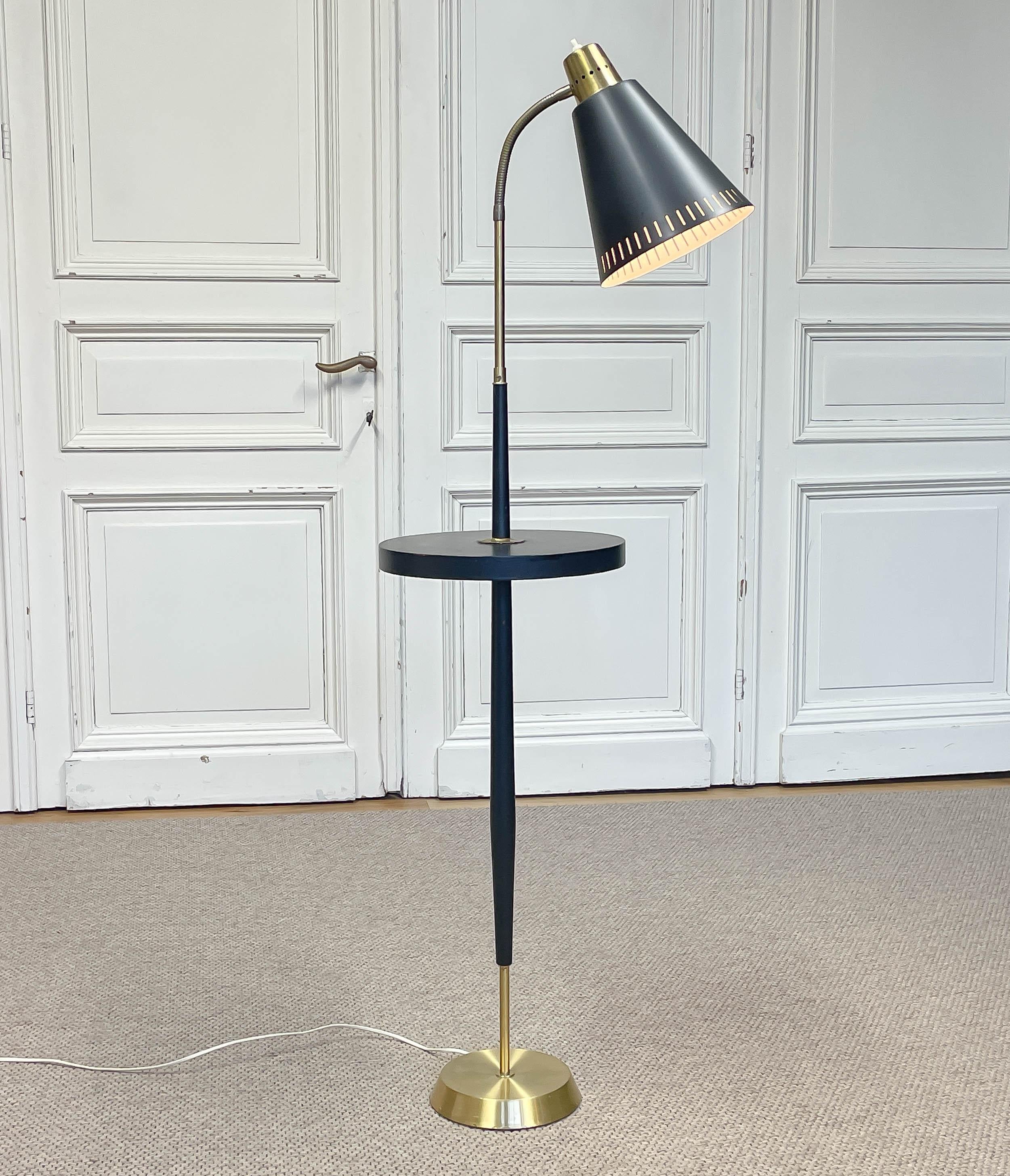 1940s, Art Deco floor lamp from Sweden.
Elegant design featuring a black lacquered stem with an integrated round side table, brass details, and an aluminium shade with decorative perforations.
Equipped with an E27/28 socket and later electrical