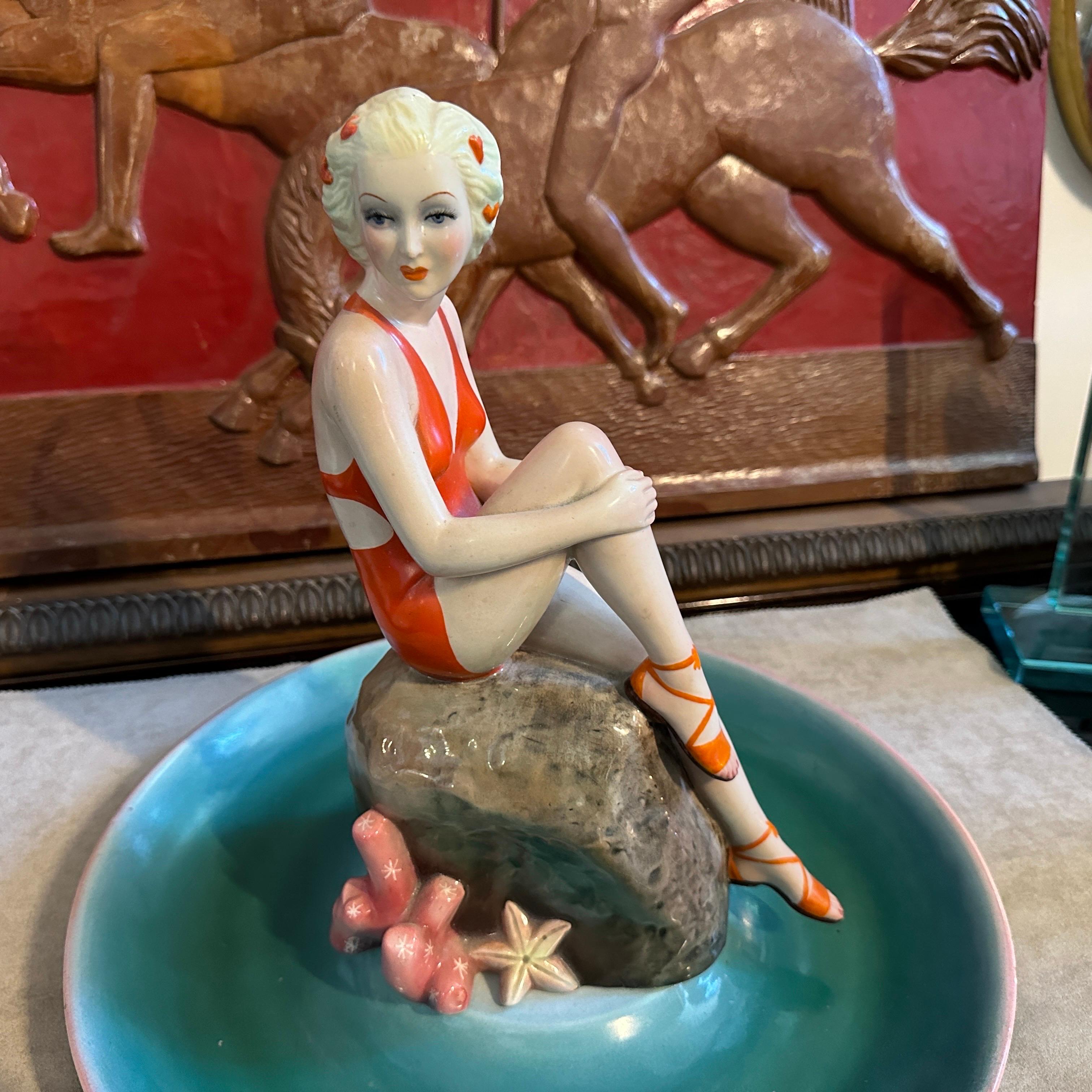 A ceramic figure of a woman at sea handmade by the famous Ronzan manufacture of Turin, the object is of superb quality, it is composed of two pieces, a round base and the figure of a woman in costume sitting on a rock. The figure it's signed Ronzan