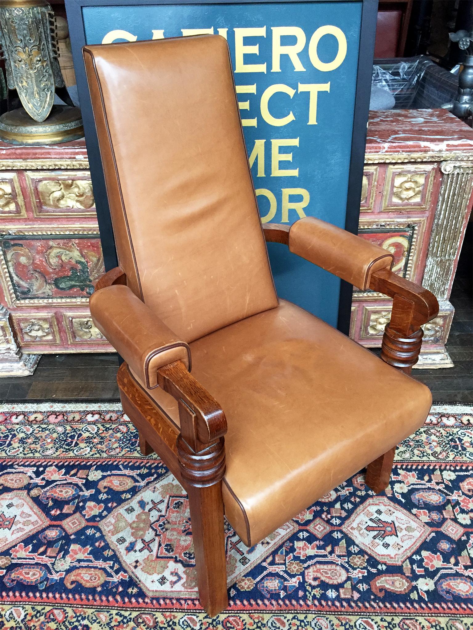 This Art Deco high-back armchair was designed by Charles Dudouyt, circa 1940s. The frame is a solid oak finished in a dark glaze, while the upholstery is a tan leather contoured by piping in a darker leather. While the design is minimalist, there