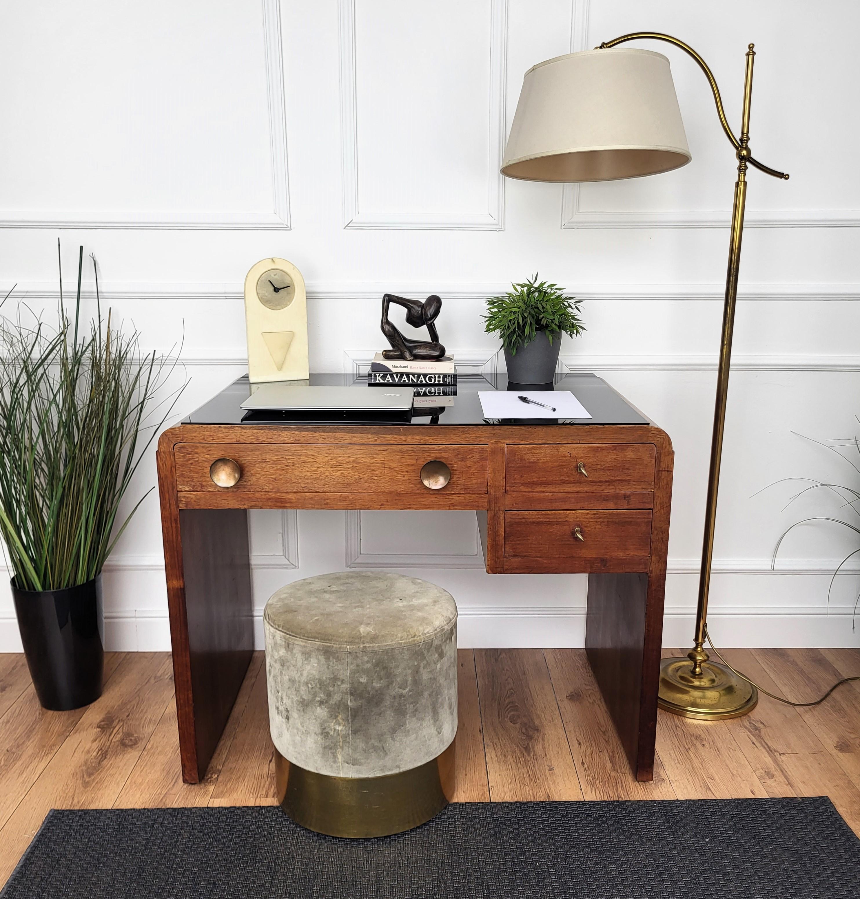 Beautiful Italian Art Deco Mid-Century Modern desk writing table, in wood with elegant carved frame, curved sides and black glass top highlighted by the three drawers with beautiful brass handles and keylocks. The unique and typical design, with the