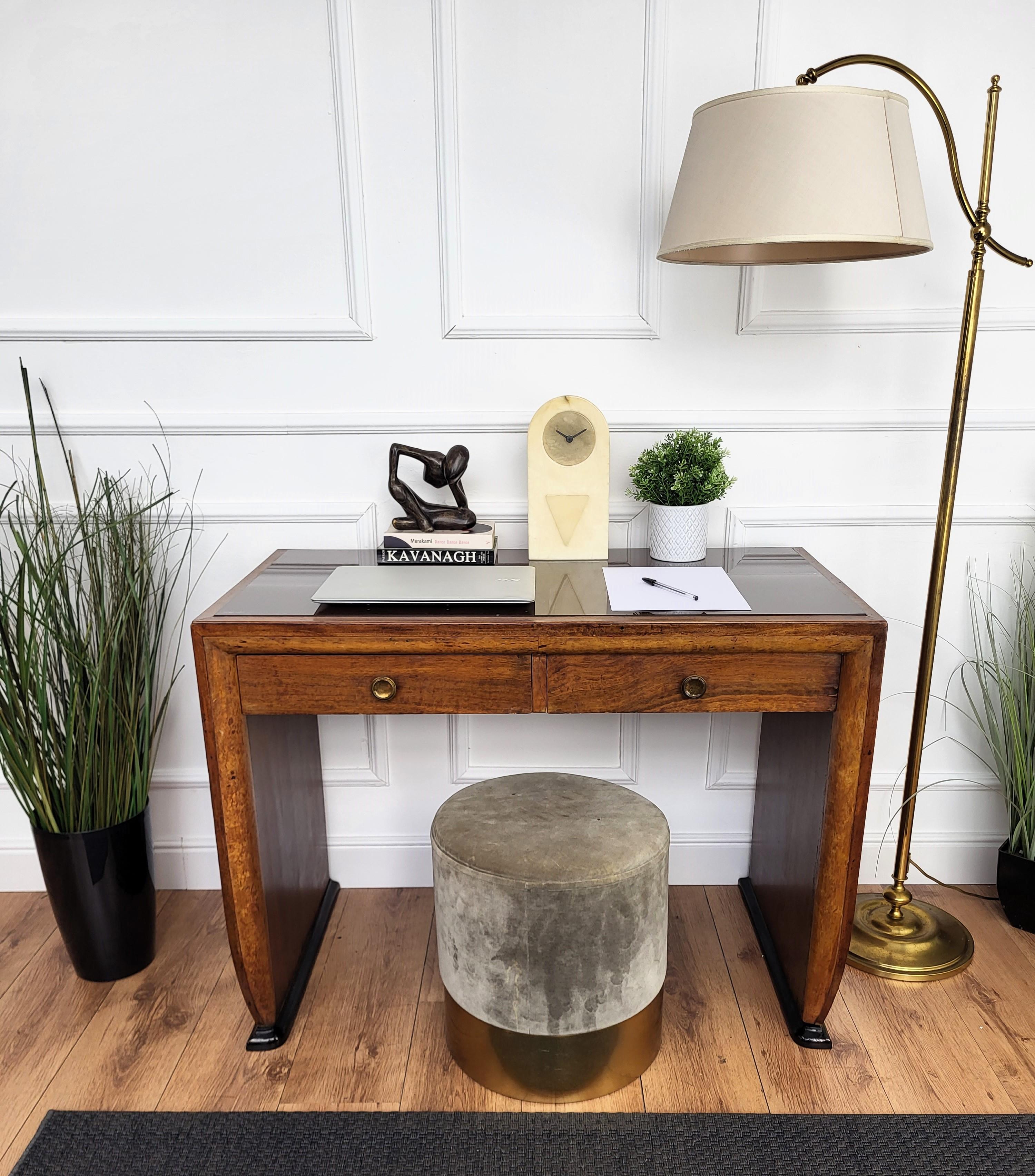 Preciosa mesa de escritorio italiana Art Decó de mediados de siglo, de madera con elegante marco tallado, lados curvados y tapa de cristal resaltada por los dos cajones con bonitos tiradores de latón. El diseño único y típico, con la forma