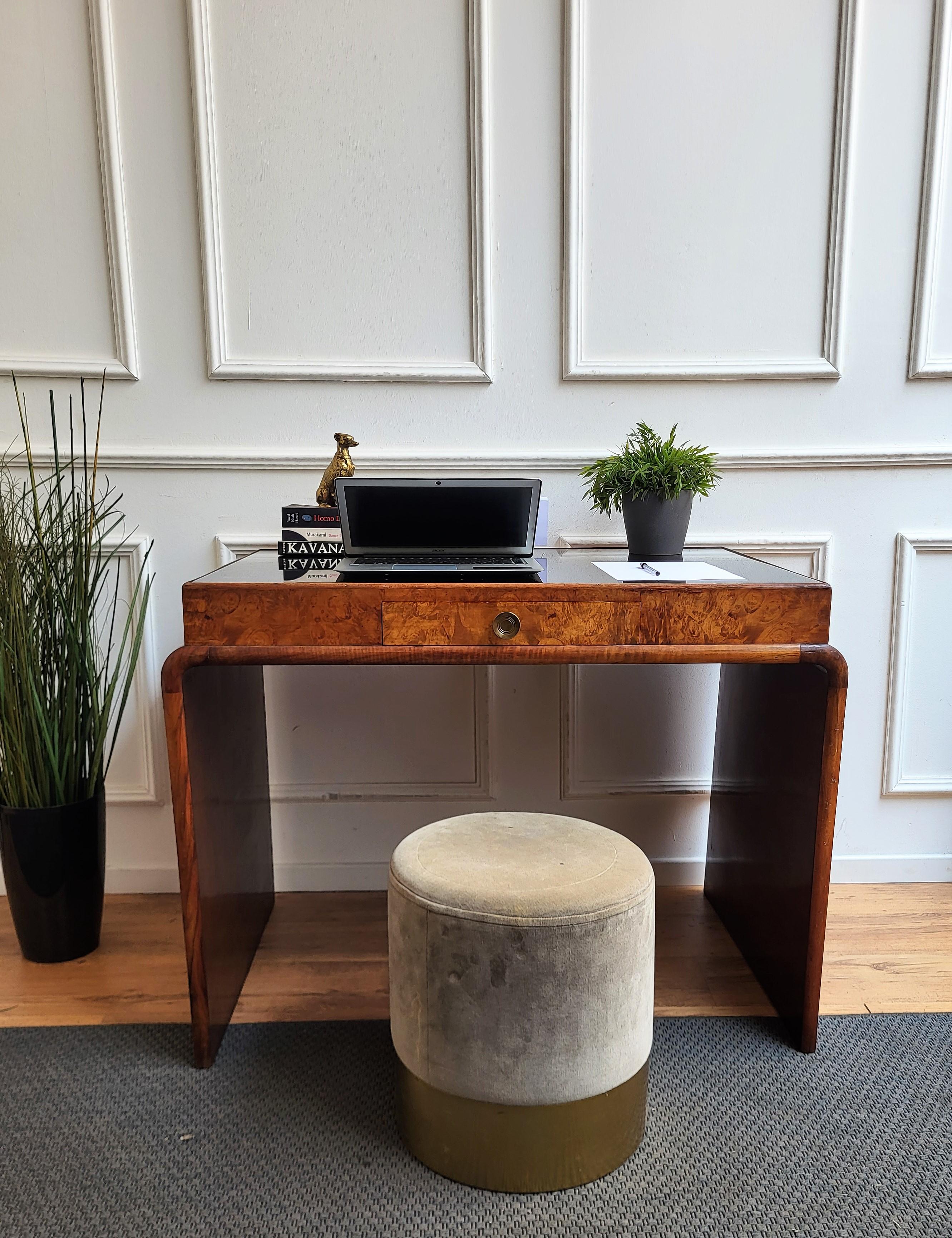 Beautiful Italian Art Deco Mid-Century Modern desk writing table, in beautiful veneer burl wood and precious black opaline glass top, with elegant carved frame and curved sides completed by the central drawers with brass handle. The unique and