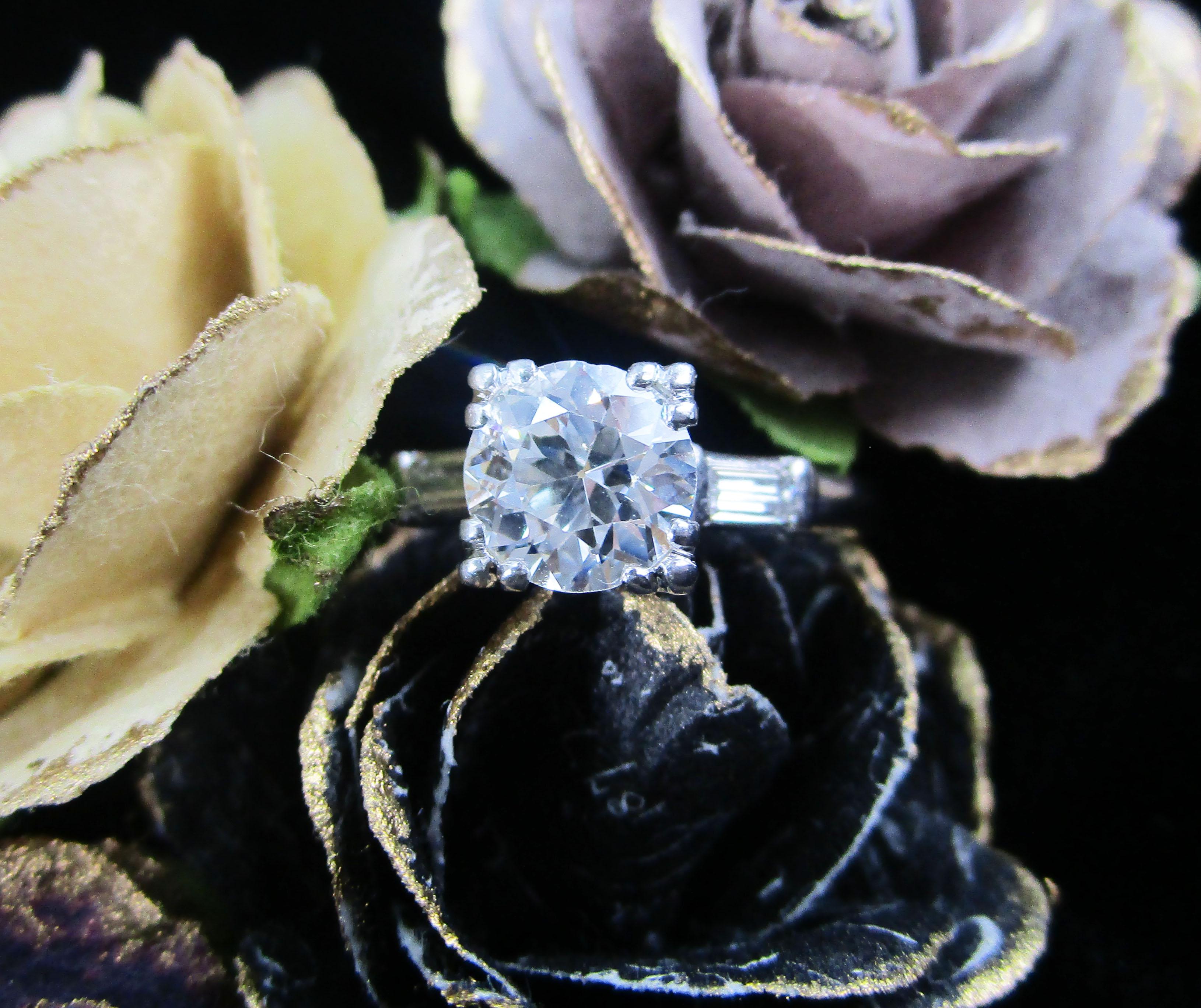 This is an absolutely gorgeous Art Deco ring in platinum with a stunning 1+ carat old Euro cut diamond center accented by two beautiful baguette diamonds! The charm of the Deco era is clear in the linear design of this ring. The two baguettes on