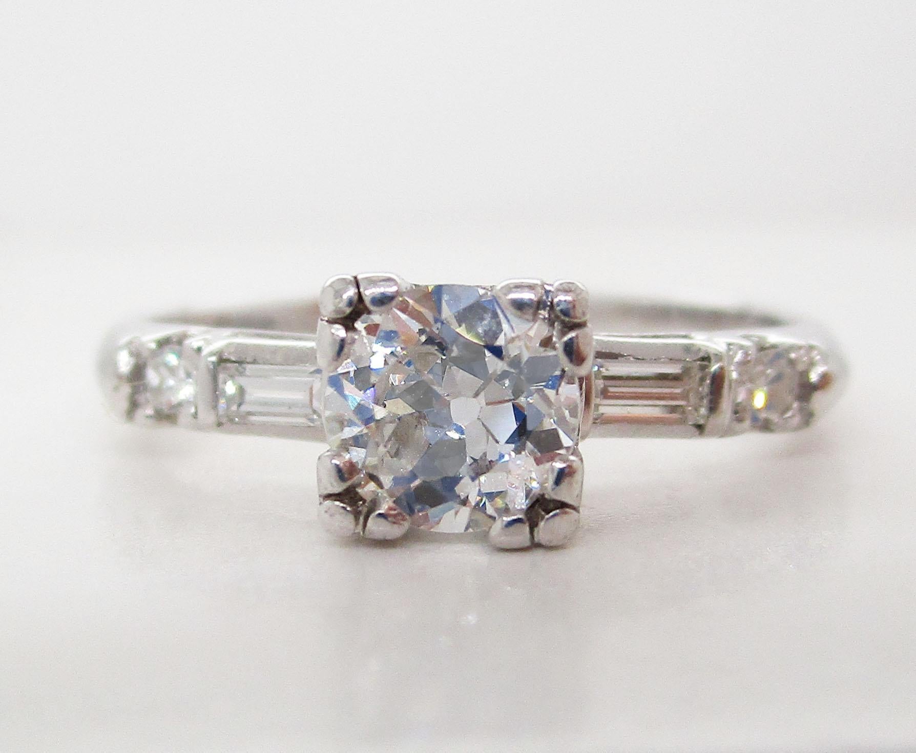 This is a gorgeous classic platinum diamond engagement ring. The ring features an absolutely stunning Old European cut diamond center that is flanked by a baguette diamond and a round diamond on each shoulder. The diamonds are almost perfectly