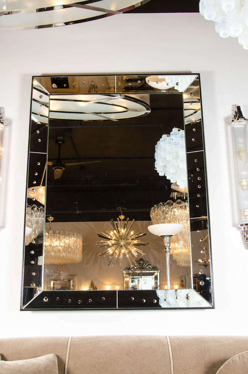 This stunning 1940s Art Deco mirror was realized in the United States circa 1945. It features an abundance of reverse etched and beveled circular detailing circumscribing the border- consisting of ten adjoined mirrored pieces- of this rectangular