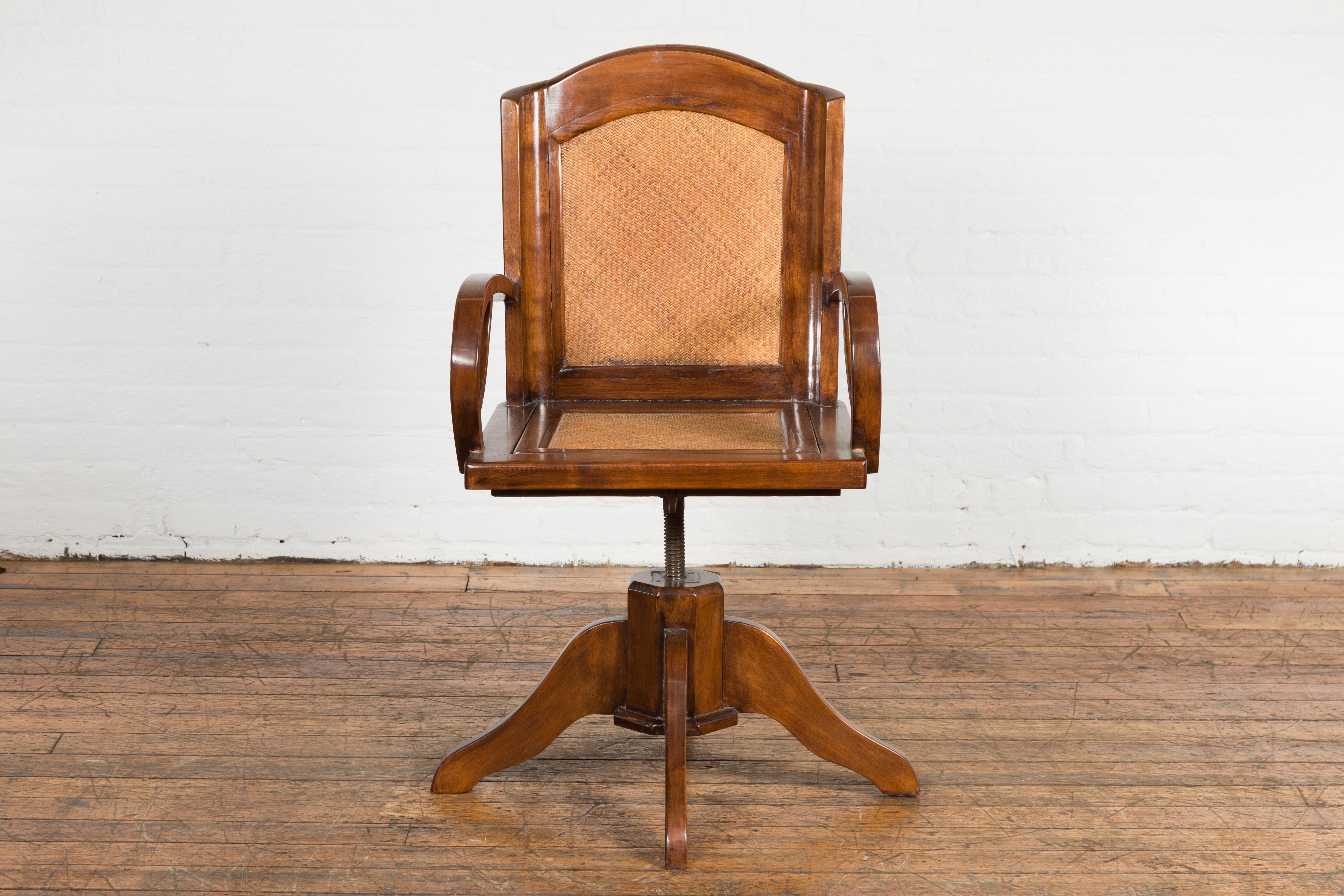 An Art Deco swivel desk chair from circa 1940 with woven rattan back and seat, loop arms and removable seat. A harmonious blend of form and function, this Art Deco Swivel desk chair from circa 1940 encapsulates the era's sophisticated aesthetic with